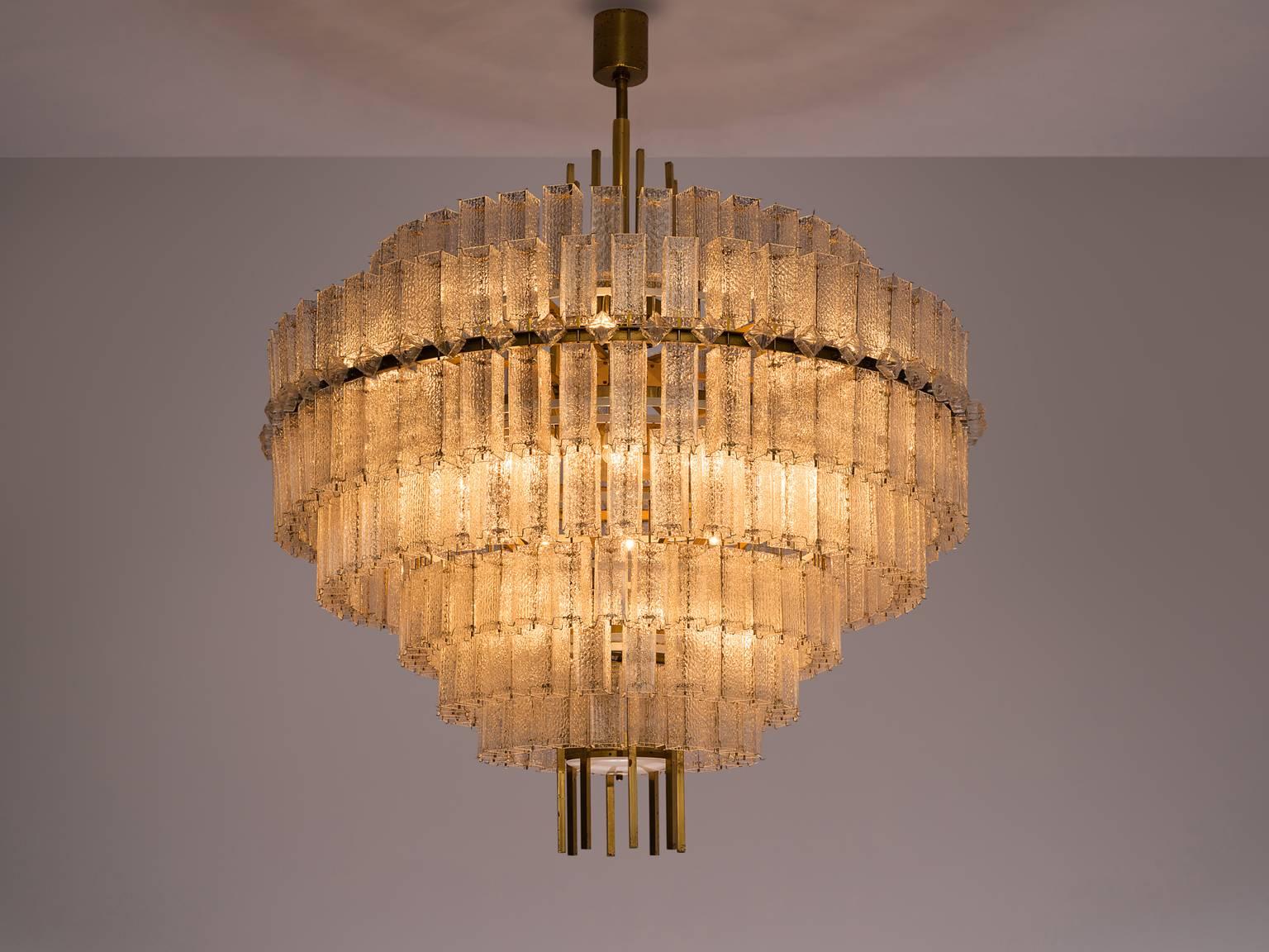 Chandelier, in glass and brass, Europe, 1970s. 

Large circular 200cm/6.5ft chandelier with seven layers of glass shades. The frame is made of brass and holds numerous structured glass 'tubes' with a brass centre. Due the combination of materials