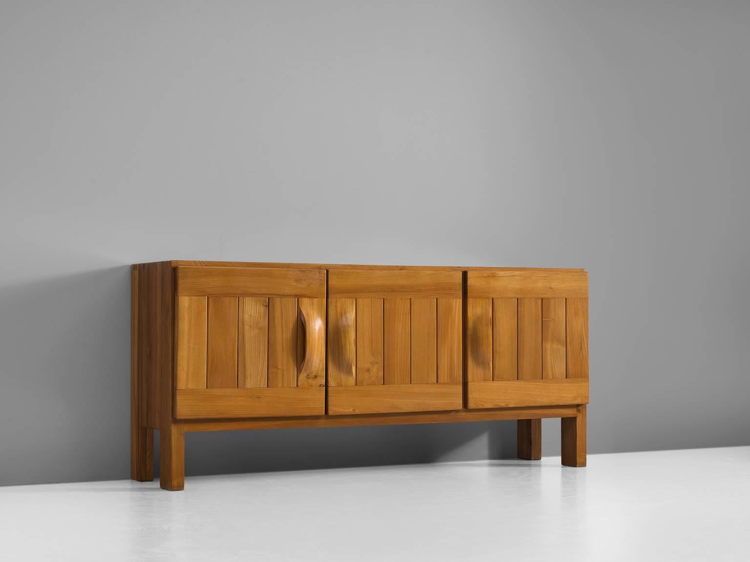 Credenza by Maison Regain, elm, France, 1960s.

This exquisite credenza combines a simplified yet complex design combined with nifty, solid construction details that characterize Maison Regain's designs. The three well balanced, sturdy doors are