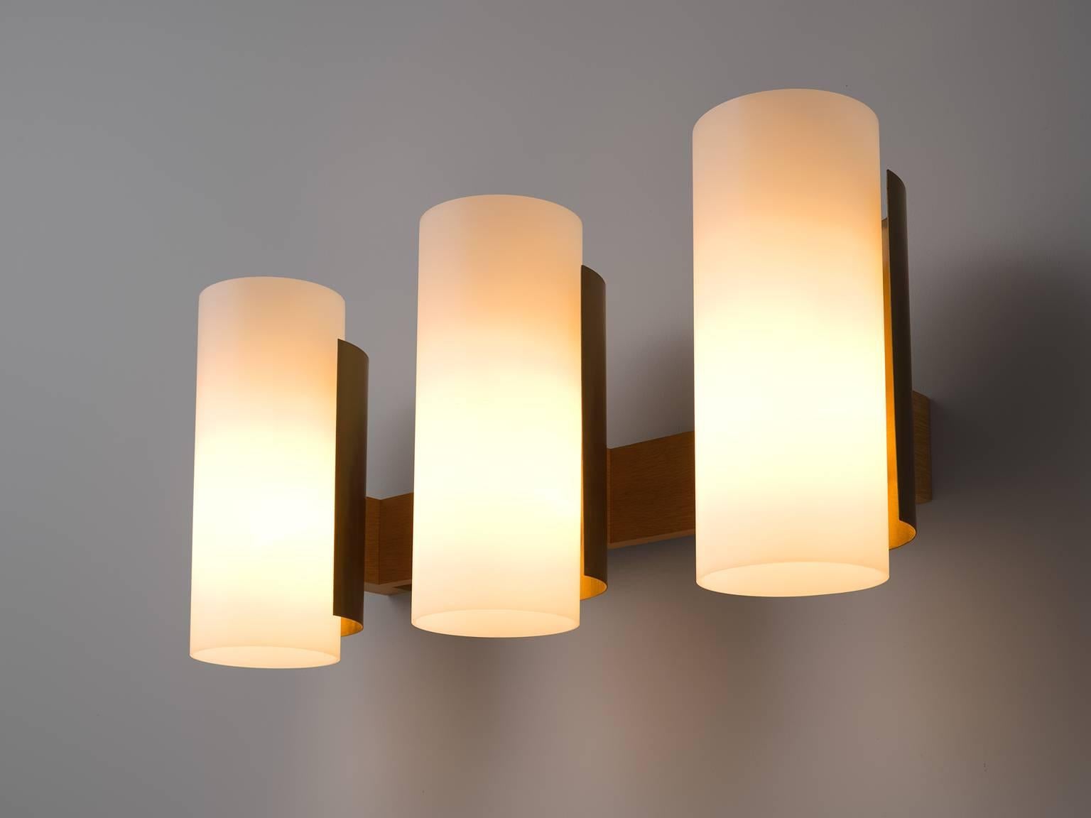 Sten Carlquis, set of three wall lights, in brass wood and polyester, Sweden, 1960s. 

Set of three large wall lights. Each light consist three cylindrical white shades, which are held by a brass frame. The wall fixture is made out of wood. The
