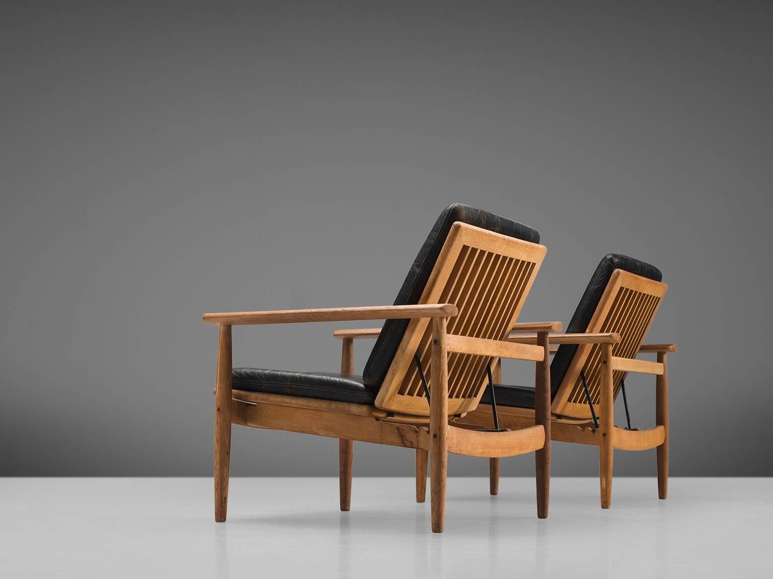Johan Hagen, armchairs, oak, black leather, Denmark, 1960s.

These modest chairs with slatted backs are executed in oak and upholstered with black leather. The back is adjustable and can therefore be put in any desired position. 
Please note that