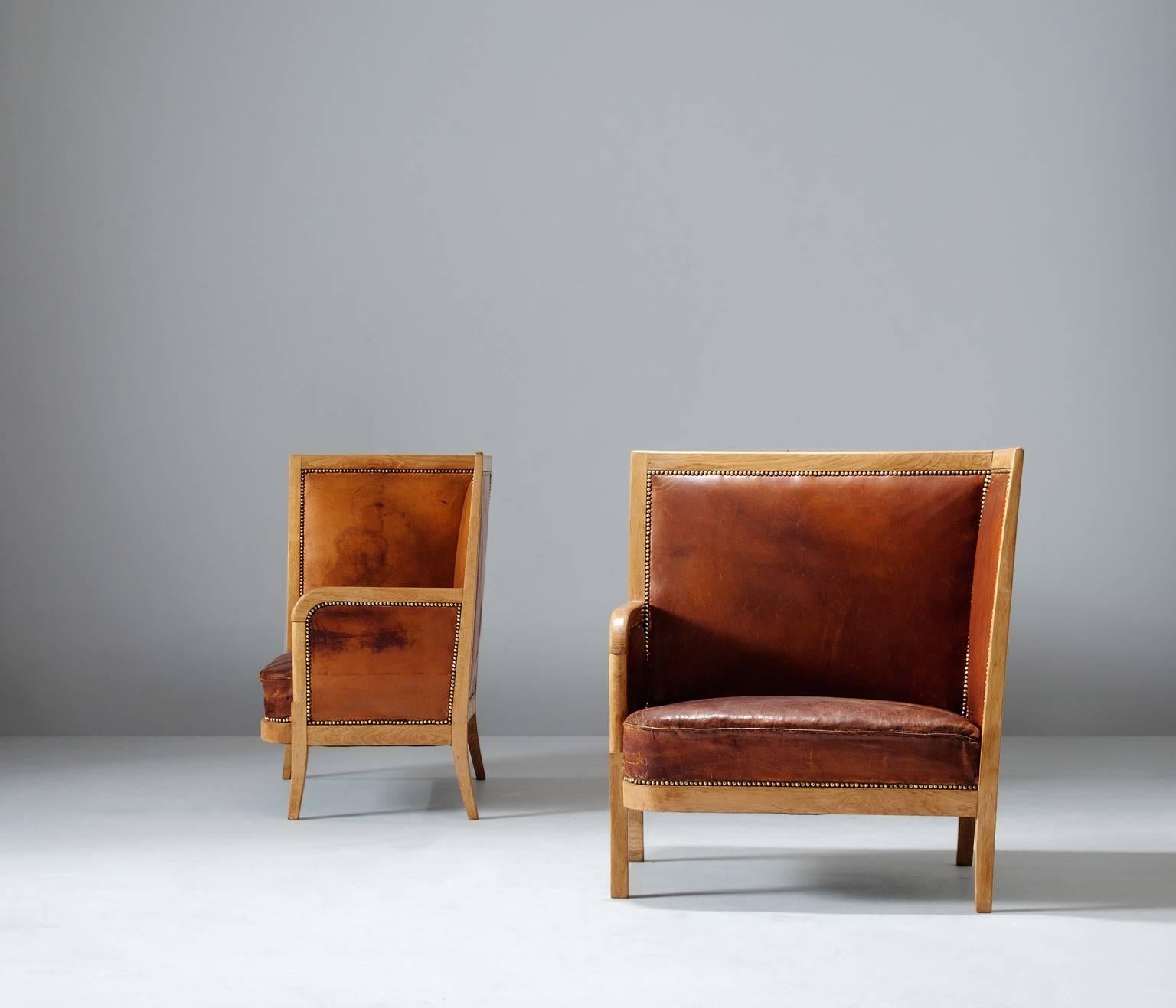 Set of two lounge chairs, in oak and leather, Scandinavia, 1940s. 

Set of two high back chairs upholstered in high quality cognac leather.
This luxurious set is made of an oak frame with nice round shapes and lines
decorated with brass studs to
