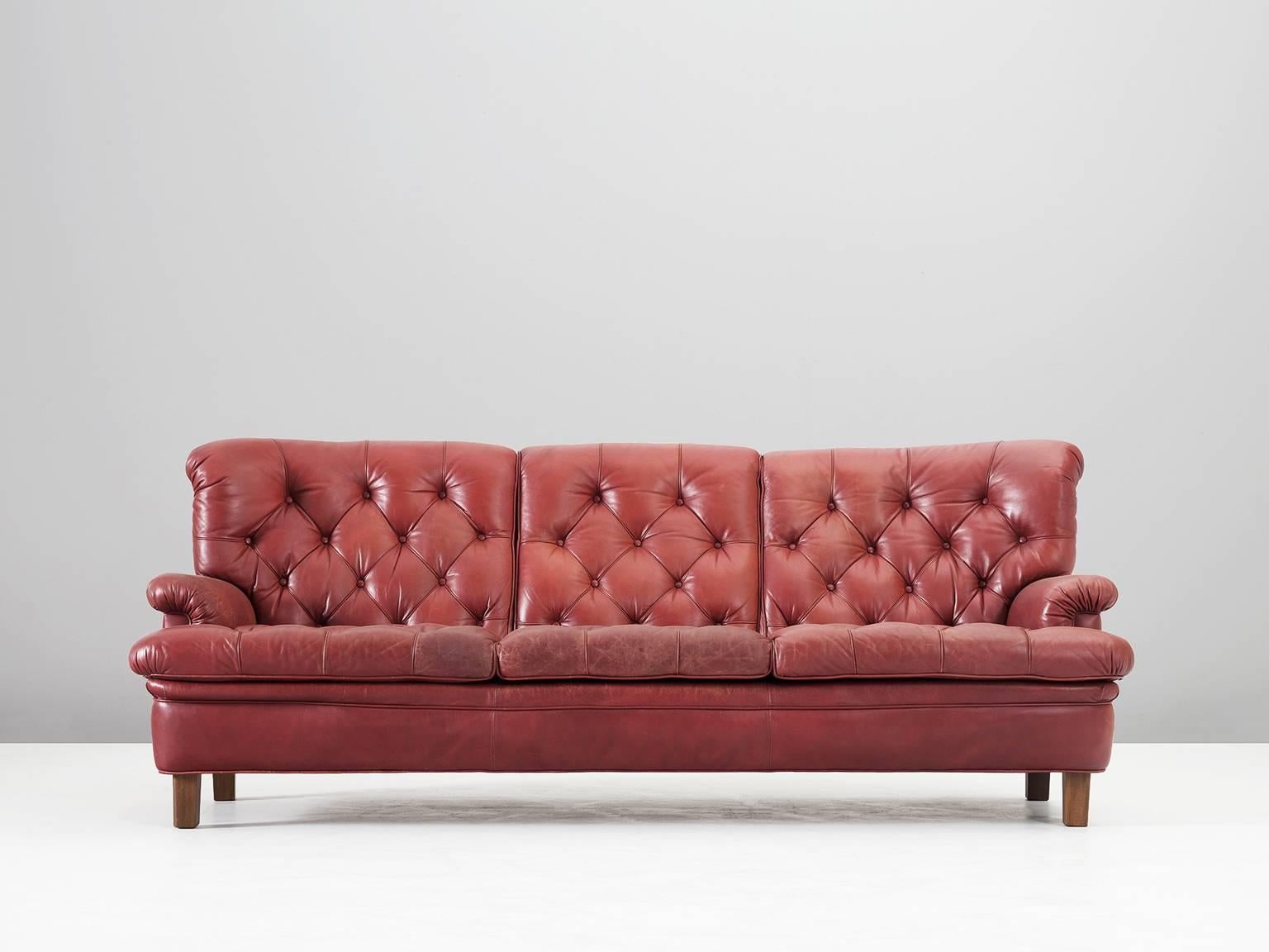 Sofa, in leather and wood, by Arne Norell, Sweden, circa 1964. 

Three-seater sofa by Arne Norell. This sofa is refined, modern and with a classical touch. A true Swedish and Norell design. The sofa is made of red leather with four cubic wooden