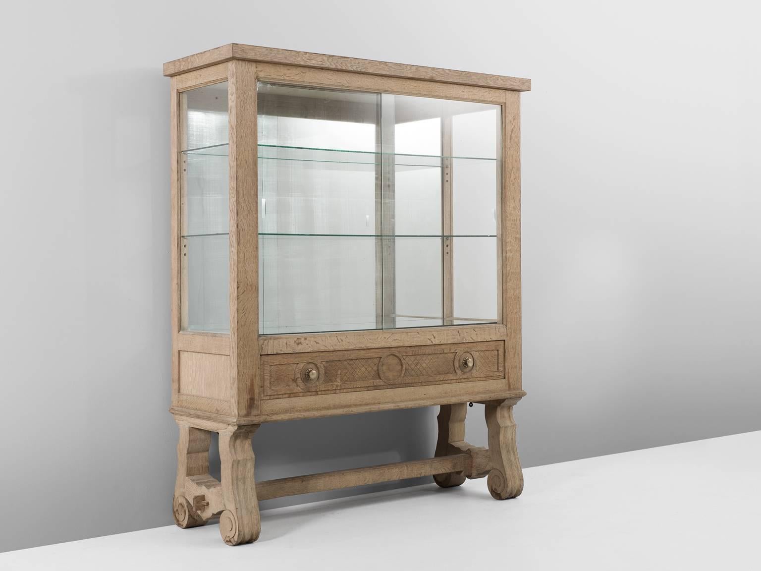 Vitrine, in oak and glass, France, 1930s. 

Vitrine cabinet in cerused oak in the style of Jean-Charles Moreux. This cabinet shows beautiful woodworking. The base consist of two beautifully wood-carved legs with a cross-connection. The cabinet