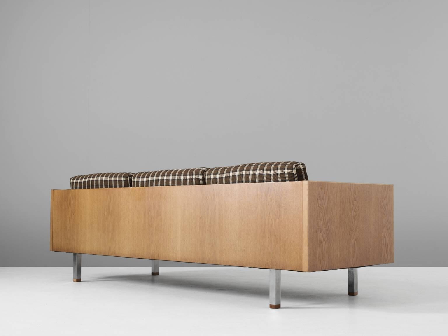 Three-seat sofa in oak, metal and fabric, Scandinavia, 1960s.

Scandinavian three-seat sofa. The frame consists of oak with cubic metal legs, which provide an open look to the quite solid seating. All sides are covered with wood and show the