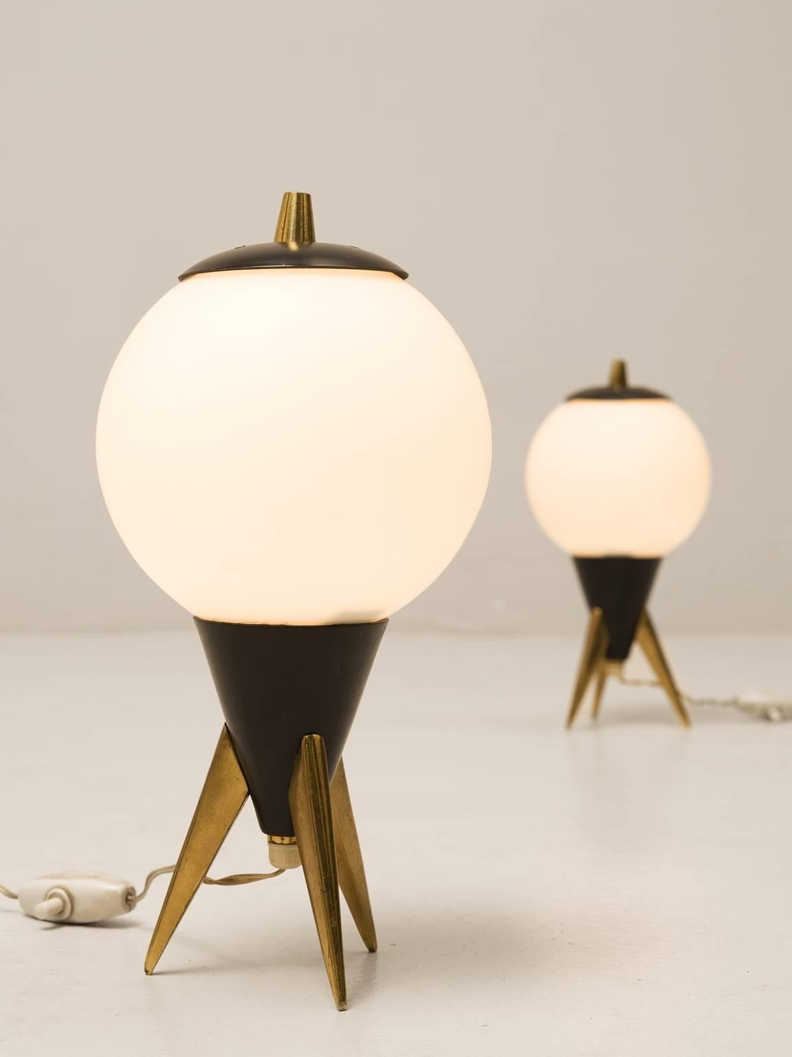 Set of two table lamp in metal, Europe, 1970s.

Two frivolous and small table lights. These lights remind of little rockets. A brass tripod base with a black coated cone, topped with a large opaline glass sphere. Each sphere has a little cap,