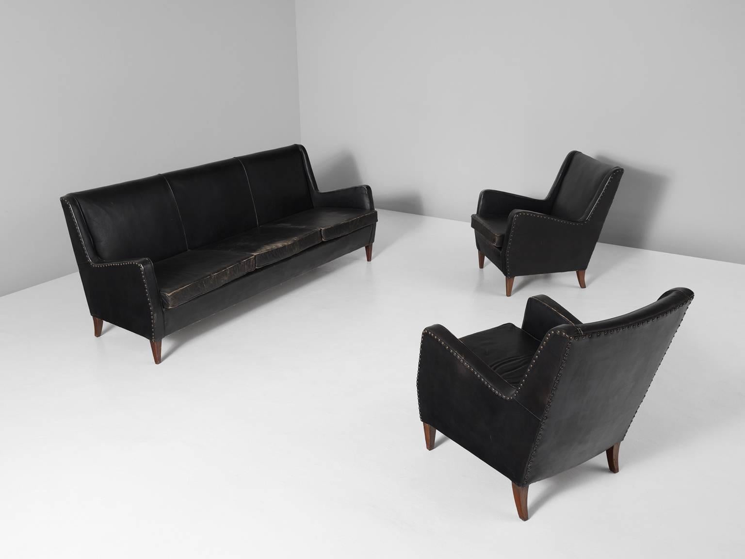 Sofa and two armchairs, in leather, brass and oak, Denmark, 1950s. 

Elegant three-seat sofa and two lounge chairs in their original leather upholstery with gorgeous patina and brass nails. This set is designed in the style of Frits Henningsen and