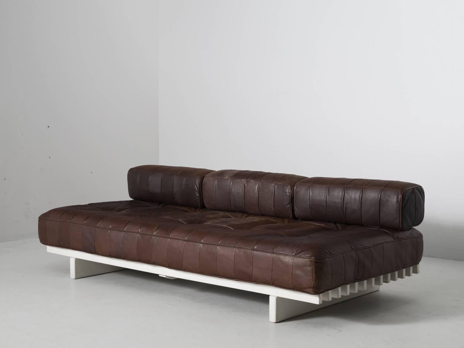 DS80 sofa, in leather and wood, by De Sede, Switzerland, 1970s. 

Daybed by the Swiss quality manufacturer De Sede. The frame consists of white lacquered wooden slats. The cushions are upholstered with brown leather in patchwork pattern. The