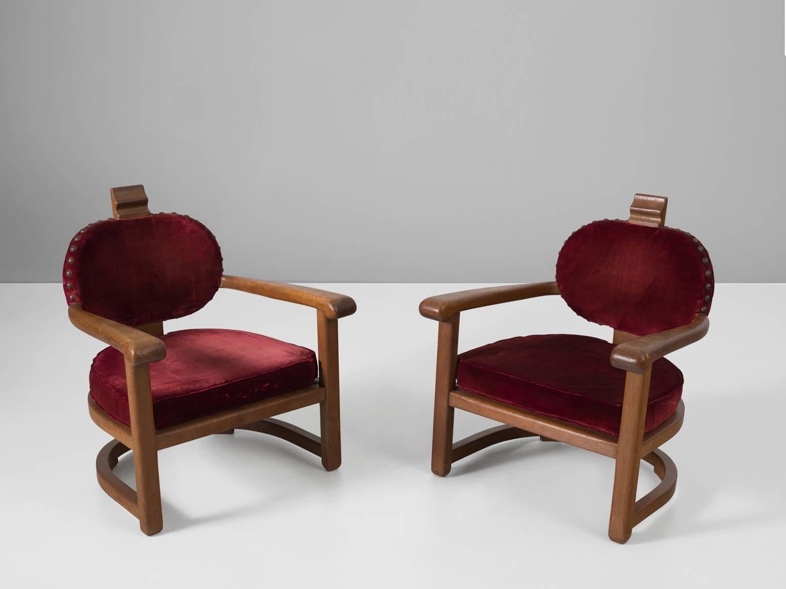 Set of two armchairs, in oak and fabric, Europe, 1930s. 

A pair of stately Art Deco club chairs with a solid oak frame and red velours fabric upholstery. Traces of age and use are visible on the fabric. We advise reupholstery. This is possible in