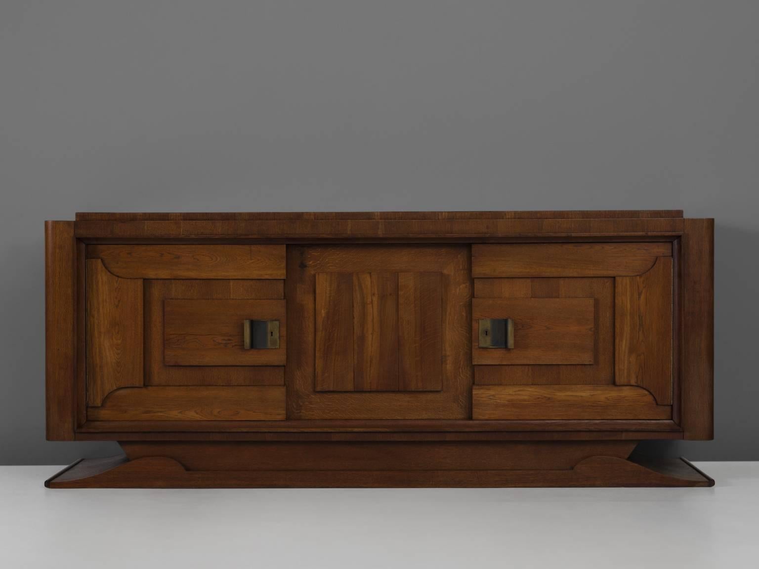 Cabinet, in oak and brass, by Charles Dudouyt, France, 1930s. 

French Art Deco oak credenza designed by the decorator Charles Dudouyt. The dark stained oak frame gives this sideboard a sturdy character. The door panels show an interesting