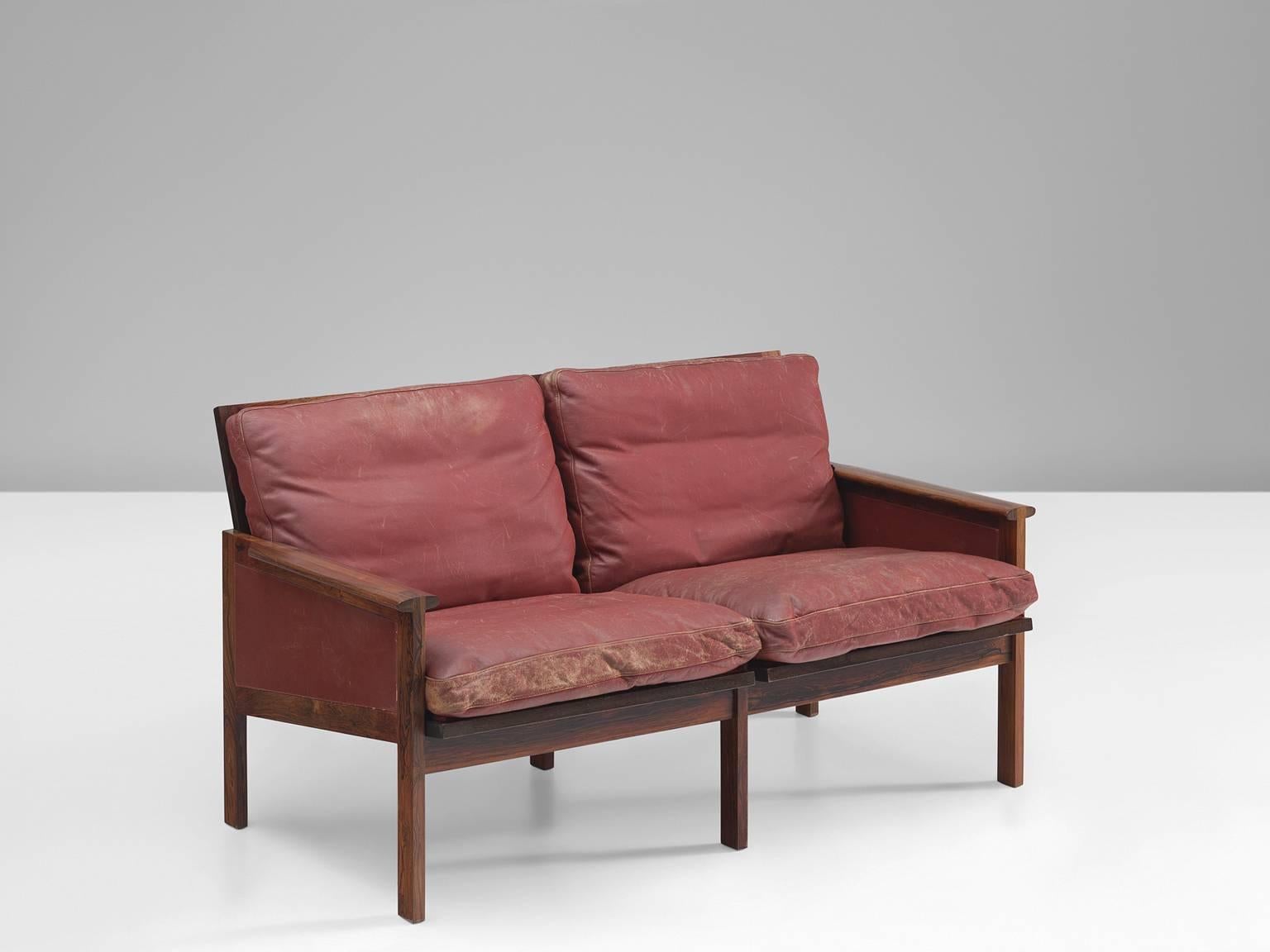 Illum Wikkelsø for N. Eilersen, two-seat sofa, red leather, rosewood, designed by Denmark, 1959.

This strong little sofa is one of the Classic designs by the Dane Illum Wikkelsø. The angular rosewood frame has six legs and and open back featuring