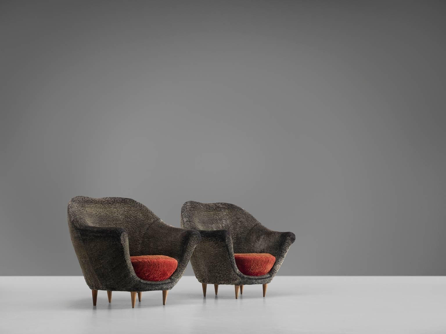 Pair of lounge chairs in grey and red velvet, wood and brass, Italy, 1960s.

This elegant, voluptuous pair of lounge chairs feature a grey to red velvet upholstery. The armrests wave outwards and the seat is a thick round cushion. The chairs stand