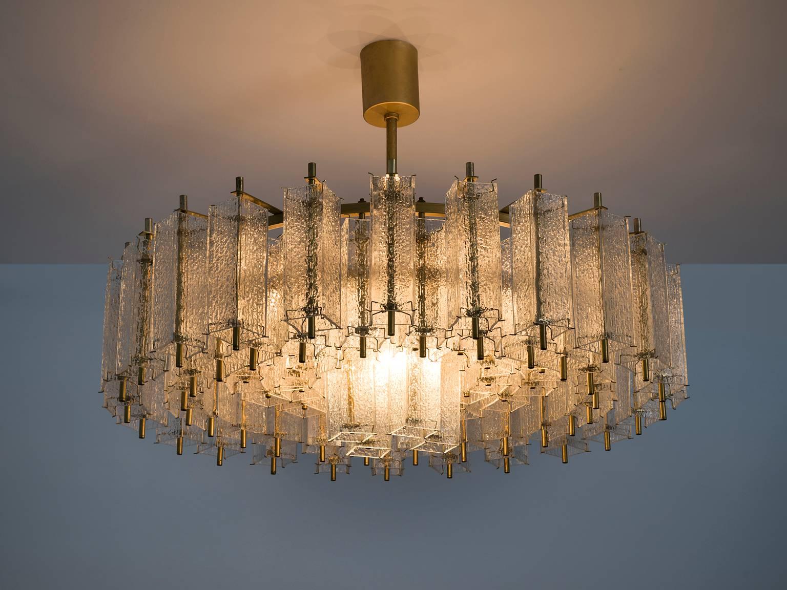 Chandelier, in glass and brass, Europe, 1970s. 

Large circular 120 cm chandelier with a great amount of glass shades. The frame is made of brass and holds numerous structured glass 'tubes' with a brass centre. Due the combination of materials and