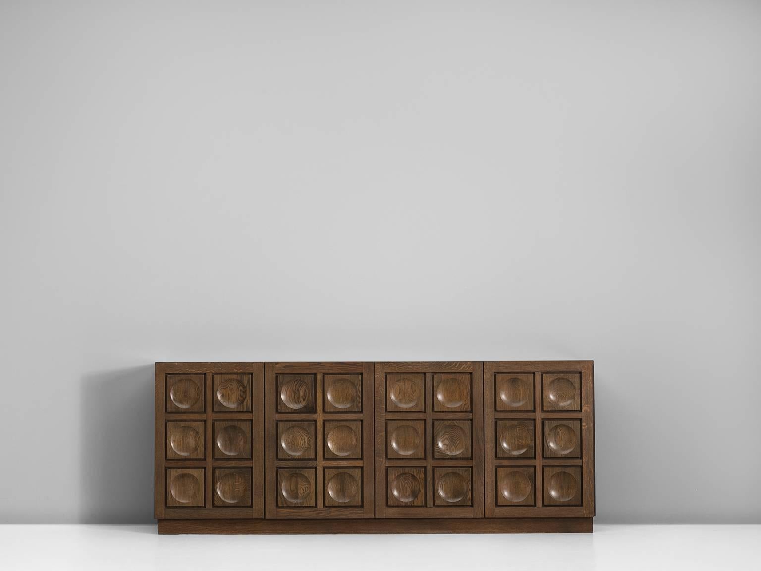 Credenza in high gloss oak, produced by De Coene, Belgium, 1970s. 

Graphical large sideboard in oak by De Coene Frères. This Brutalist credenza shows a beautiful graphical front. Each of the doors is ribbed and decorated with circles. Therefore a