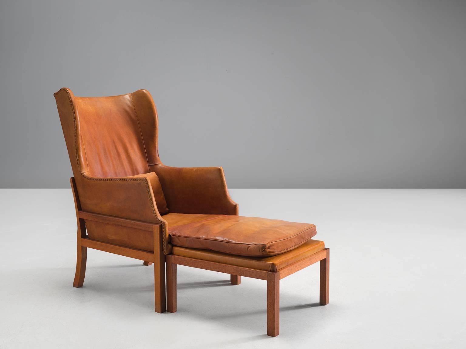 Mogens Koch for Ivan Schlechter, wingback chair and ottoman, cognac leather, mahogany, Denmark, design 1936, manufactured 1970.

Elegant and comfortable armchair in mahogany and leather by Mogens Koch. This lounge chair was designed with high