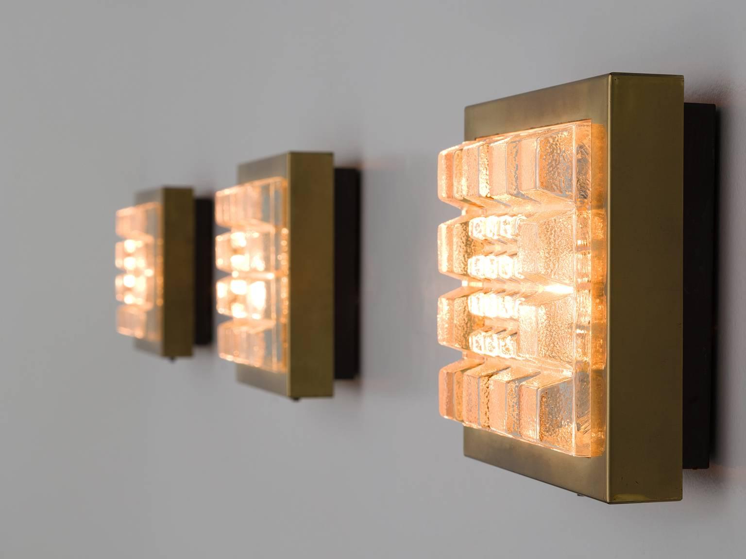 Wall lights, brass and structured glass, Belgium, 1930s.

These Art Deco wall lights are solid and sculptural. The square sconces have protruding structured glass squares in a brass frame. The light source which is behind the glass surface gives of