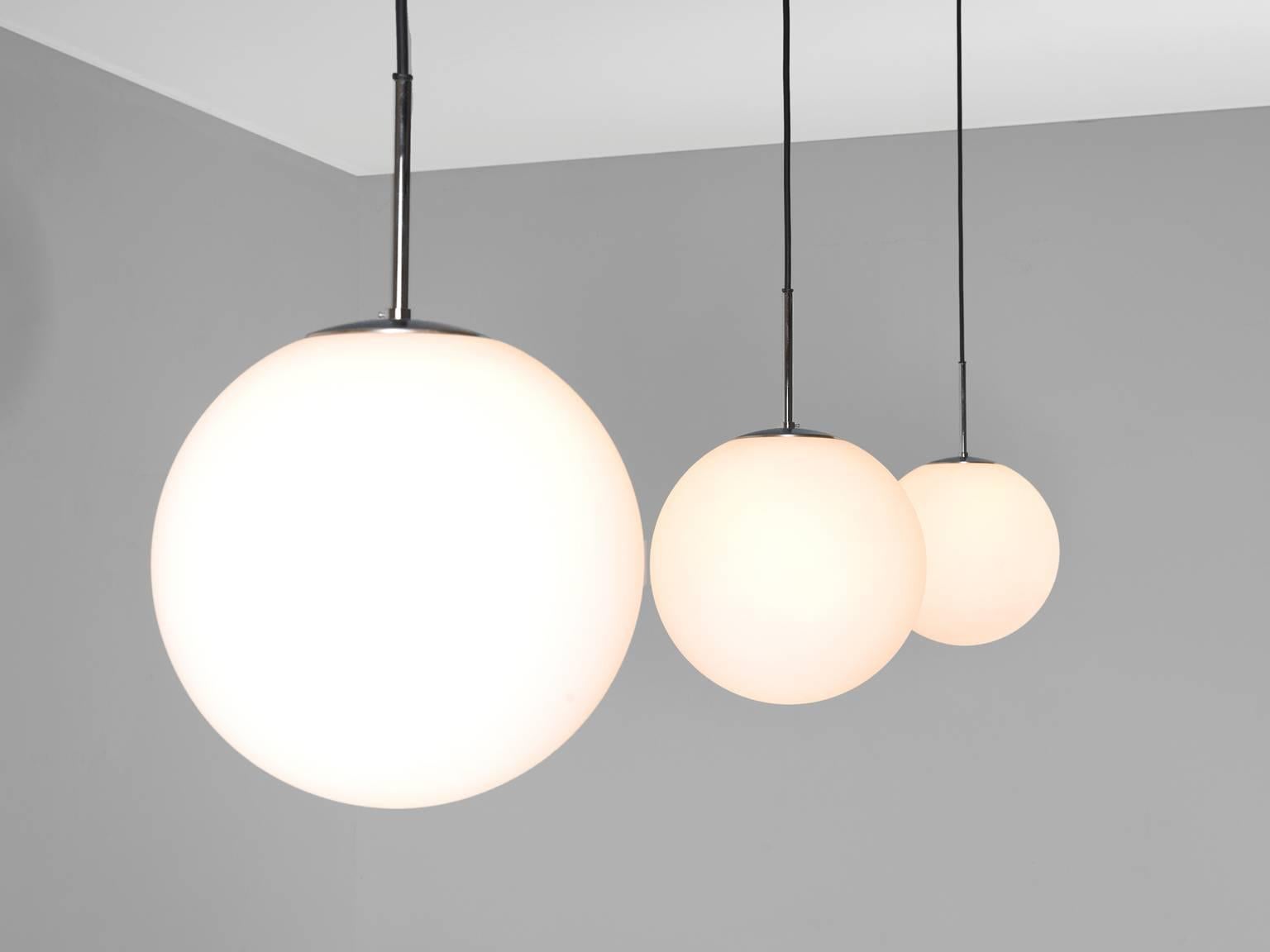 Set of three pendants, in glass and metal, Europe, 1970s.

Set of three modern pendants with white opaline glass globe shaped spheres. The round glass pendants are typical for midcentury lighting as they are softly and delicate and at the same