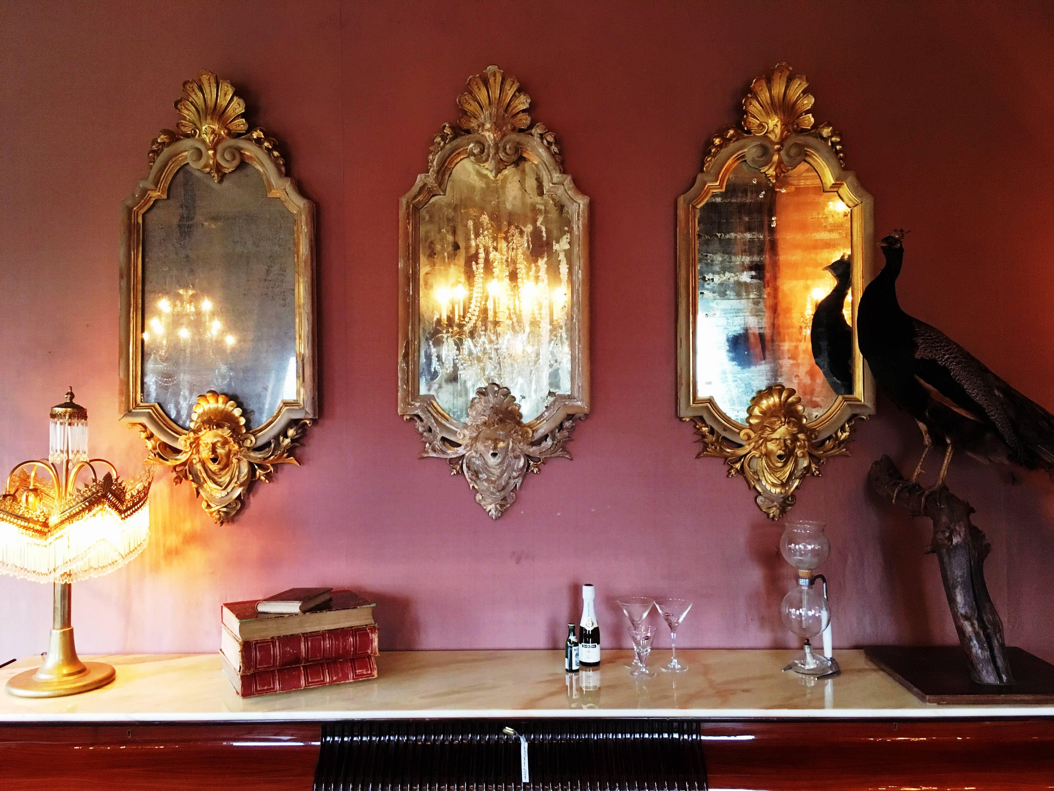 Beautiful antique mirrors in a richly carved frame decorated with a female head on the bottom and a large ornament on top.