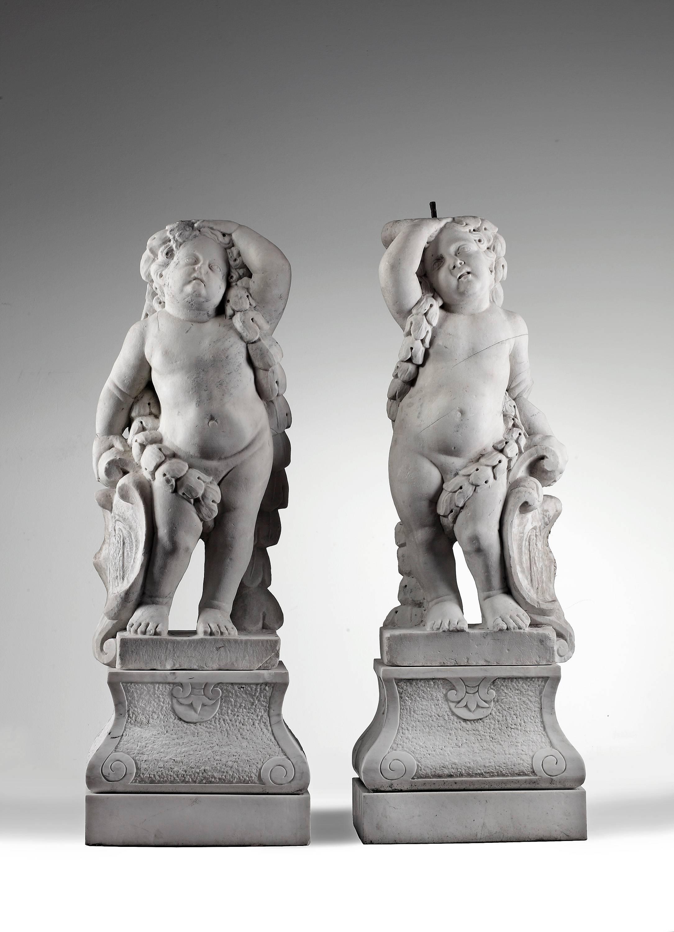 These putti were made in the late 17th century by a Flemish artist.
The putti are portrayed standing opposing and nude. They each have a floral garland draped from one shoulder and around the back. They both have a shield with a coat of arms. They