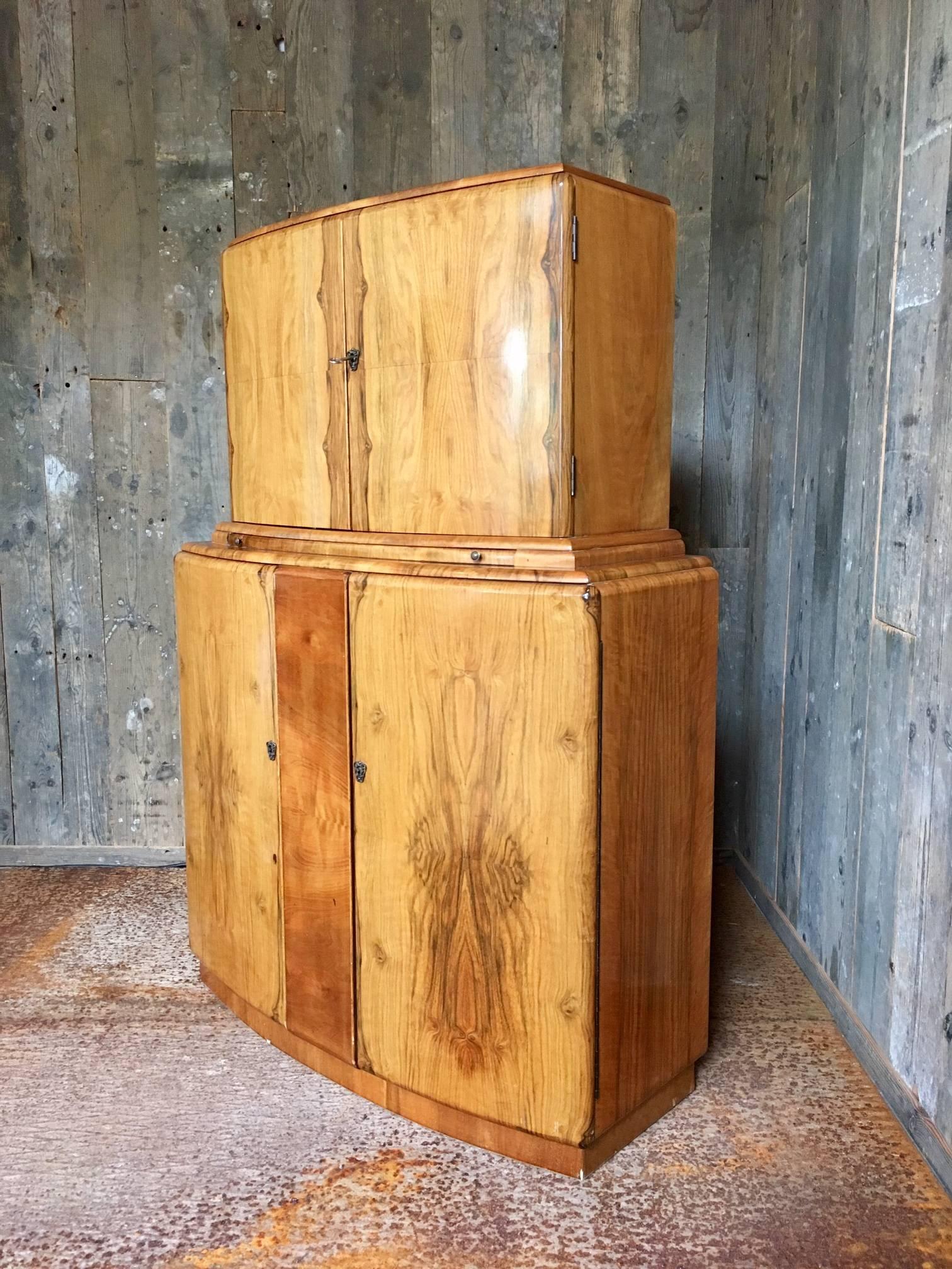 Beautiful cocktail cabinet in Art Deco style made in the 1950s by Rivington London. The cabinet is made from wood with a juglans veneer finish. The cabinet has four doors. The upper interior is covered with mirrors and a lamp lights up when opening