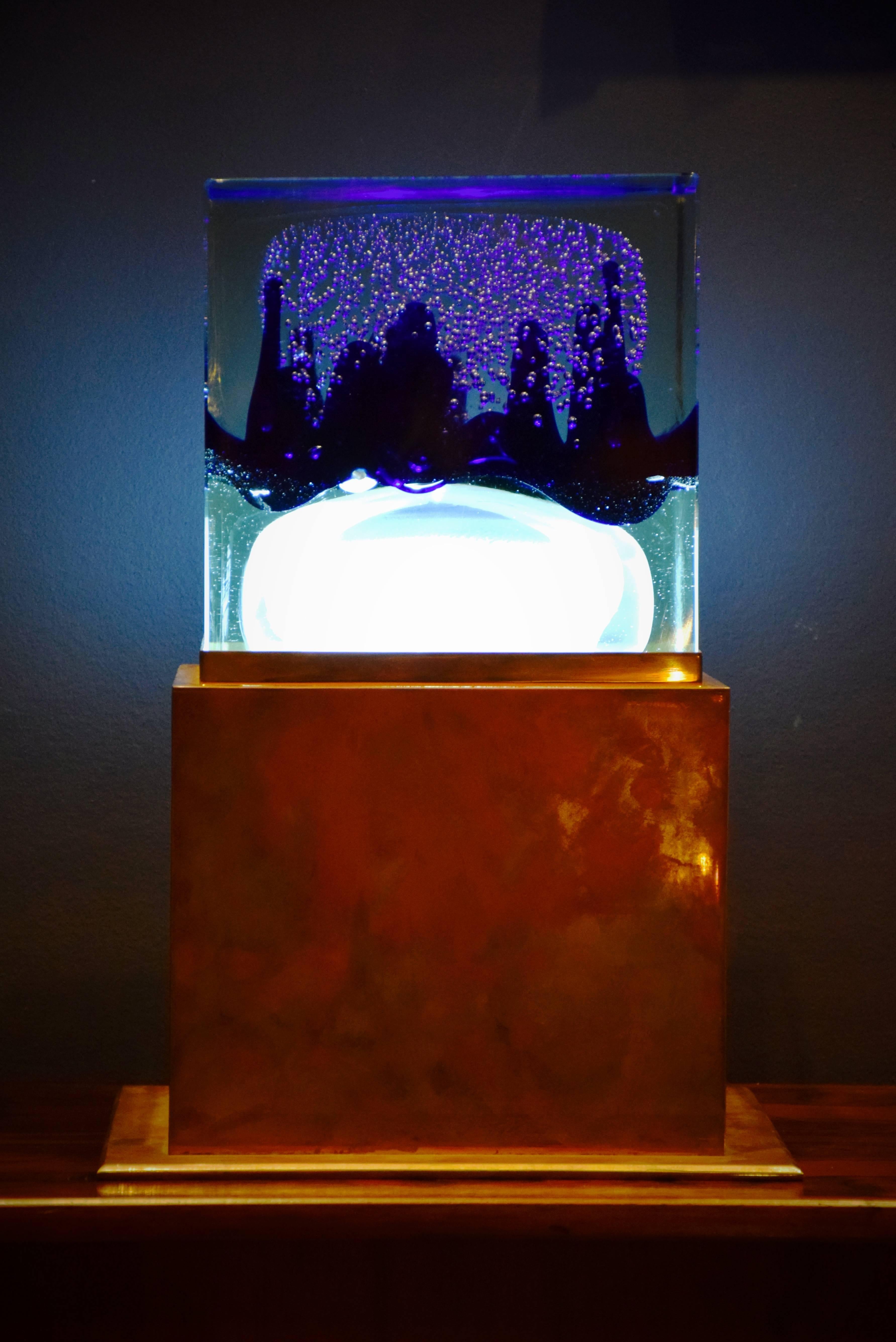 Beautiful and unique table lamp in Murano glass and copper.
The solid glass cube is filled with bubbles, blue glass and white glass in a jellyfish or cloud shape. Underneath the glass cube is a light.
The base is made from 