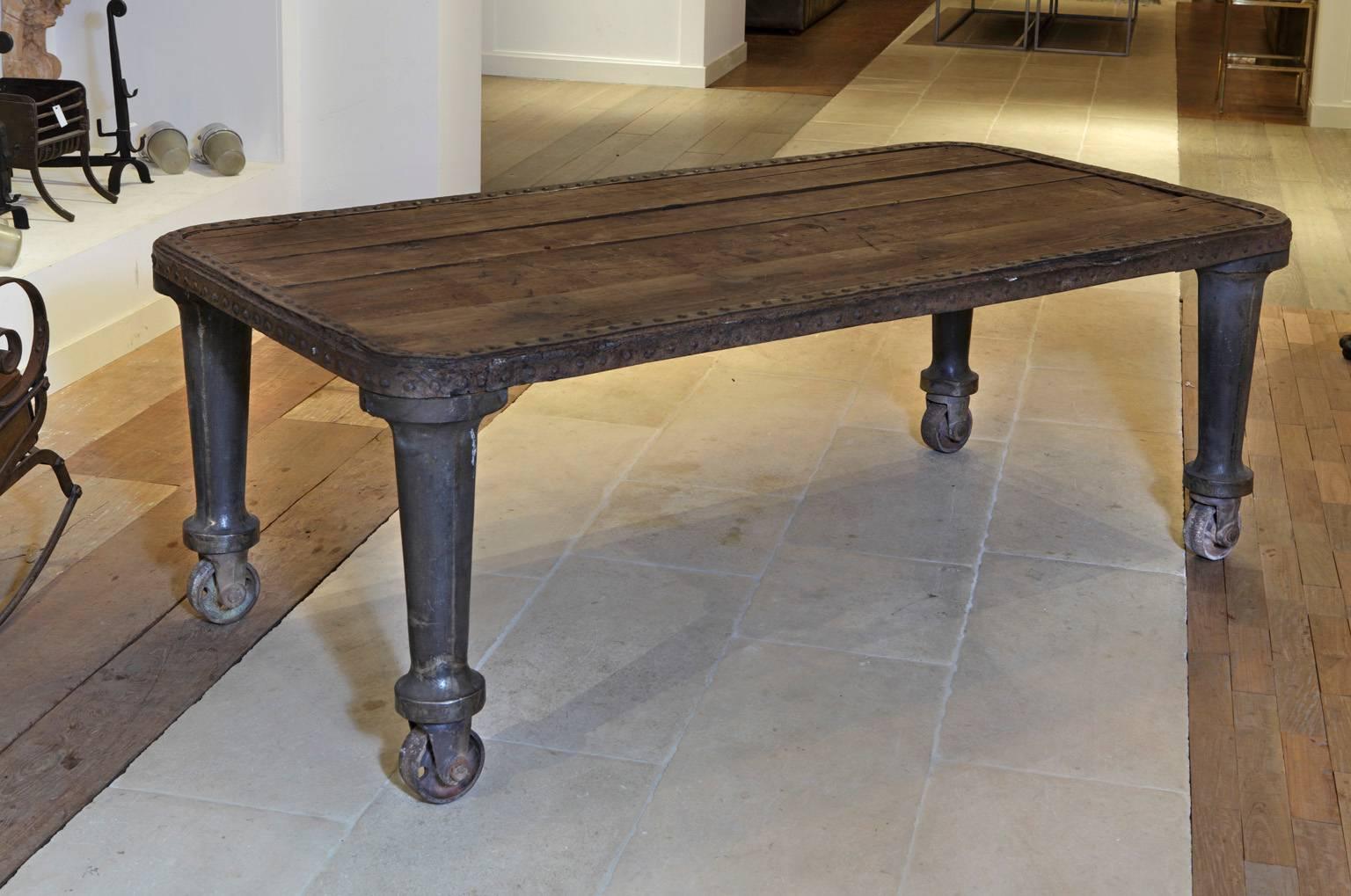 An old French Industrial dining, work or conference table on four cast iron legs and wheels, the pinewood top encased in a wrought and riveted iron frame, Machine Age, circa 1900.