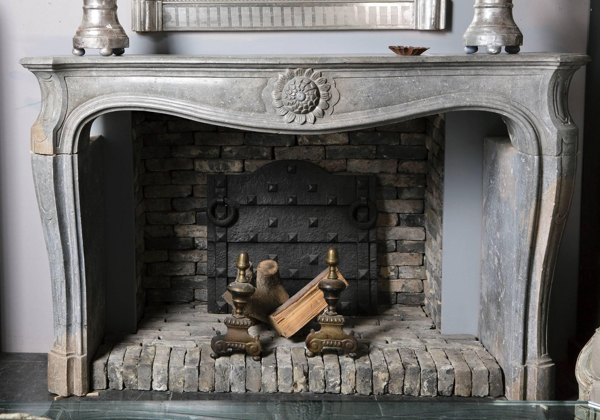 This antique fireplace is made of a rare grey shade of Pierre de Bourgonge stone from France.

The mantel is decorated with a beautiful sunflower, the symbol of Louis XIV, also known as 