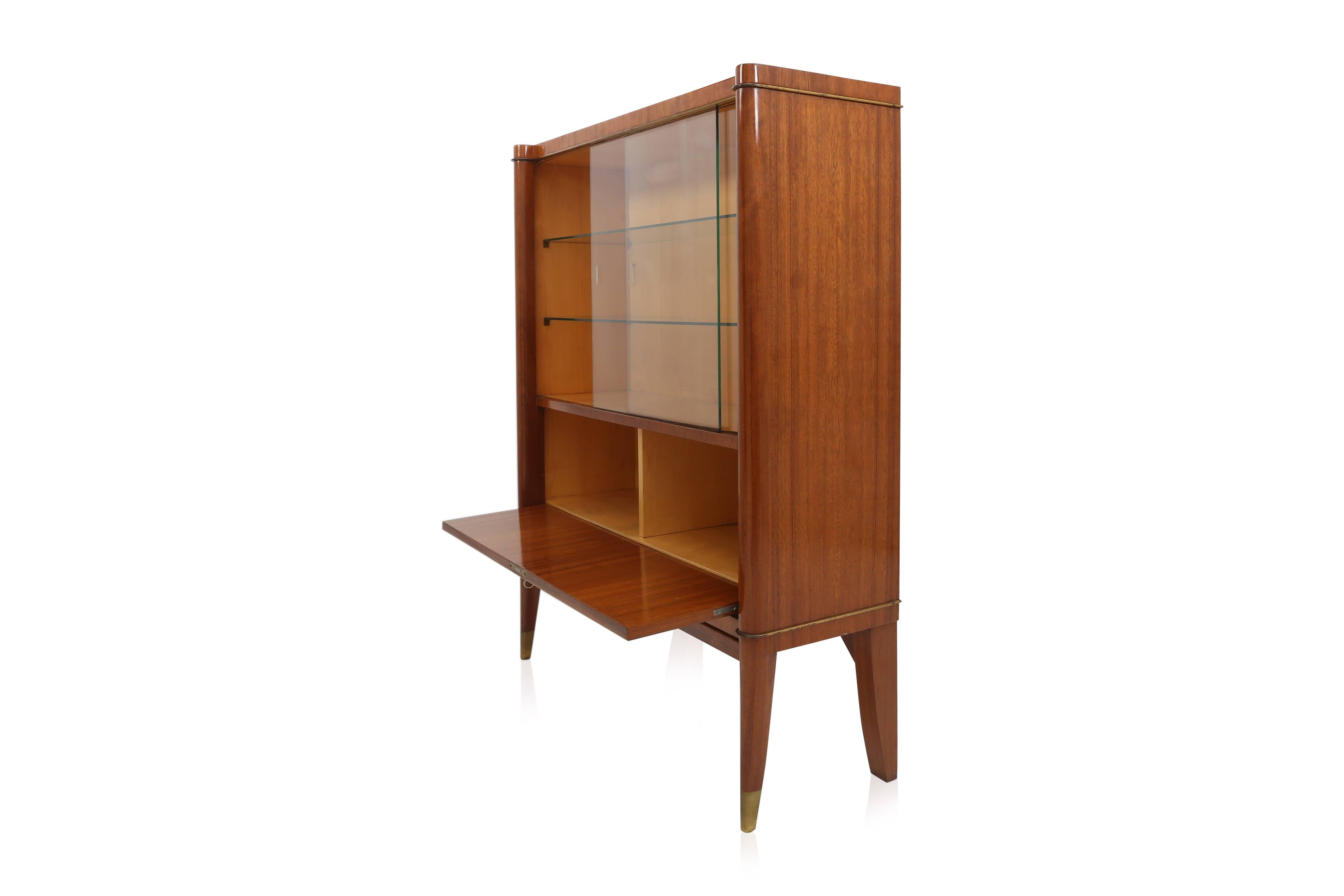 Art Deco vitrine bar cabinet from the Voltaire Gamma. 
De Coene Frères, Belgium, circa 1950.

Mahogany, gilded bronze medaillon and brass sabots.
In original state and condition.

Measures: D 32 cm W 102 cm H 130 cm.

  