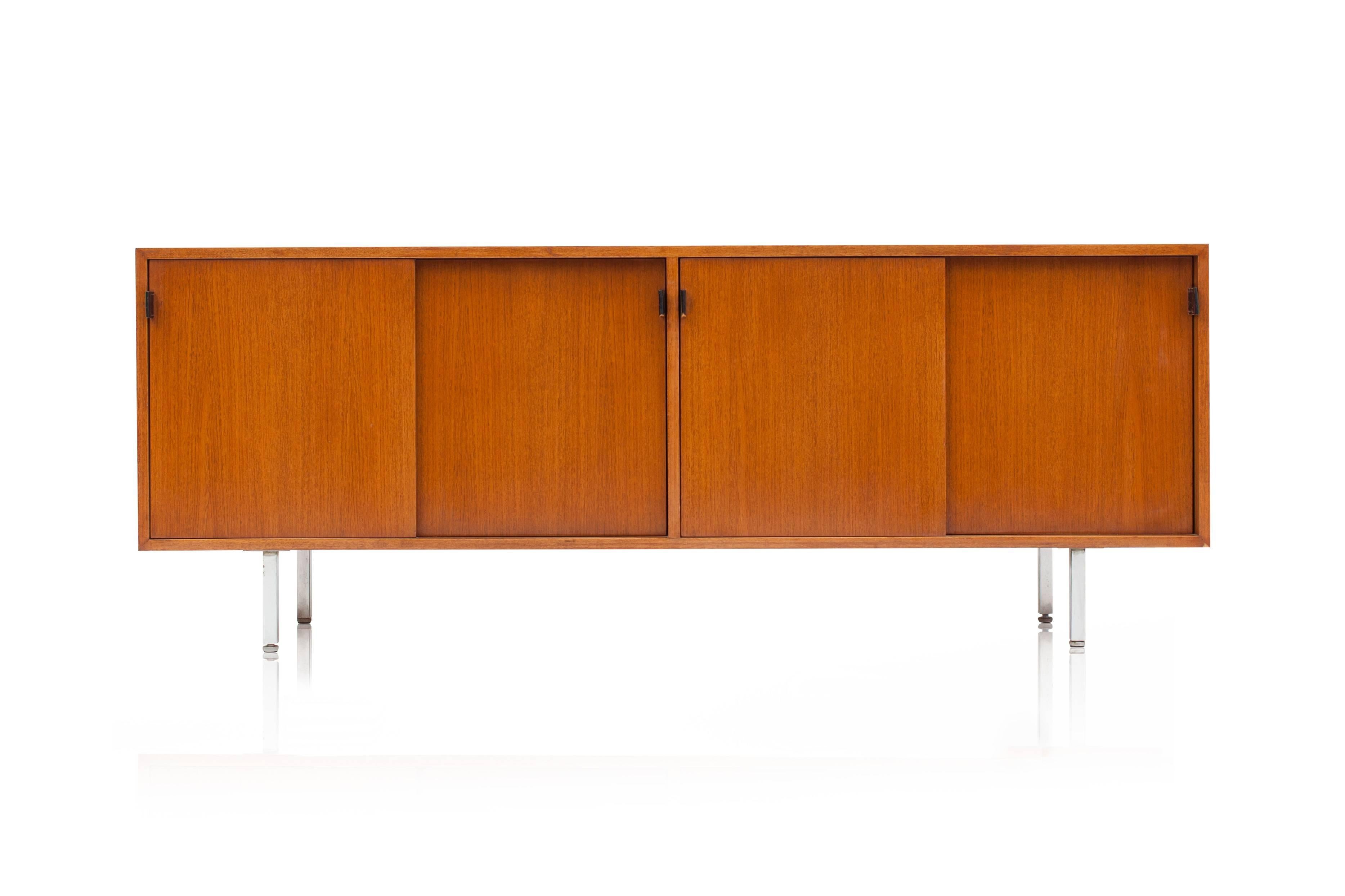 Modern credenza in teak. The credenza has four sliding doors, each provided with
elegant and beautifully patinated black leather door handles. The cabinets rest on four chrome legs. Please note that the back of the credenza's is also fully equipped