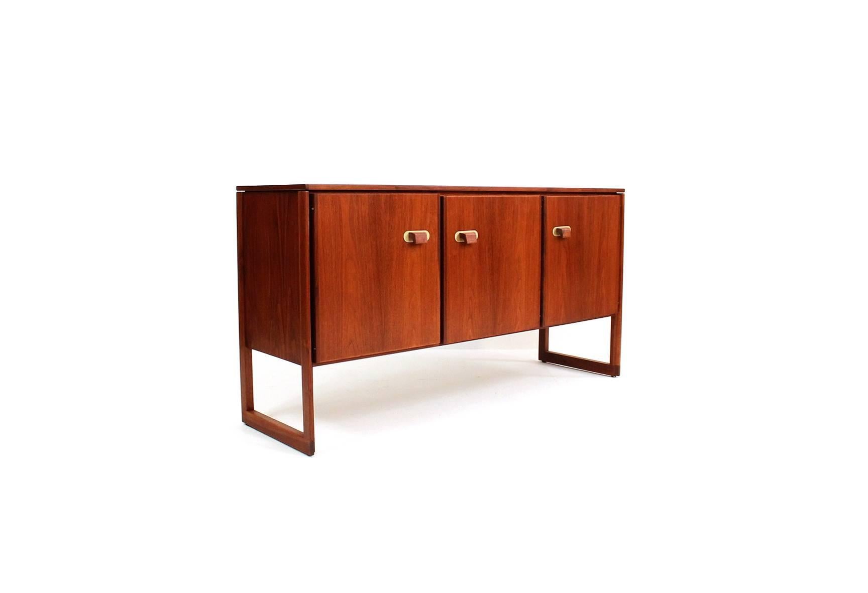Walnut credenza or cabinet designed by Jens Risom. Cabinet features sculptural solid walnut and brass pulls concealing three compartments with adjustable shelves.