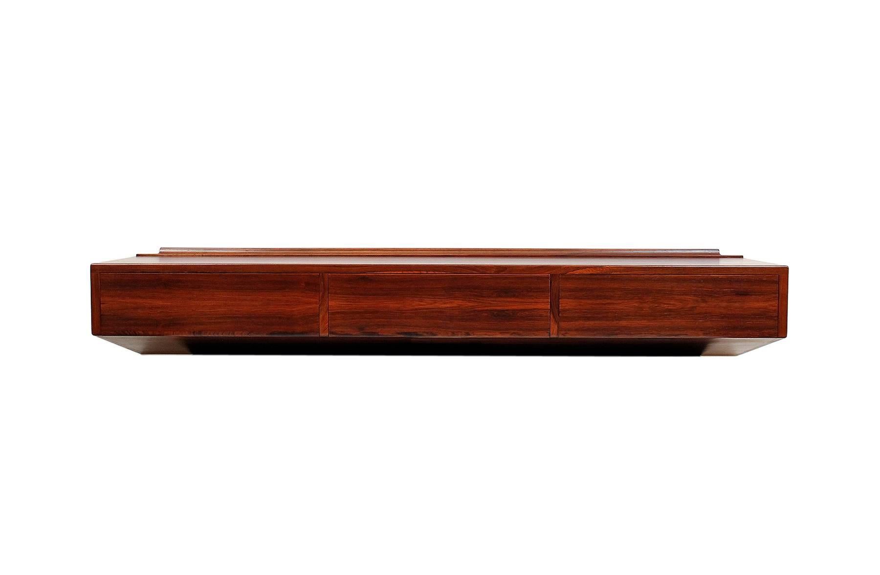Architectural wall-mounted console or desk by Danish designer Arne Hovmand Olsen. This piece features figured rosewood veneers and three drawers, one with partitions. Simple and functional design.