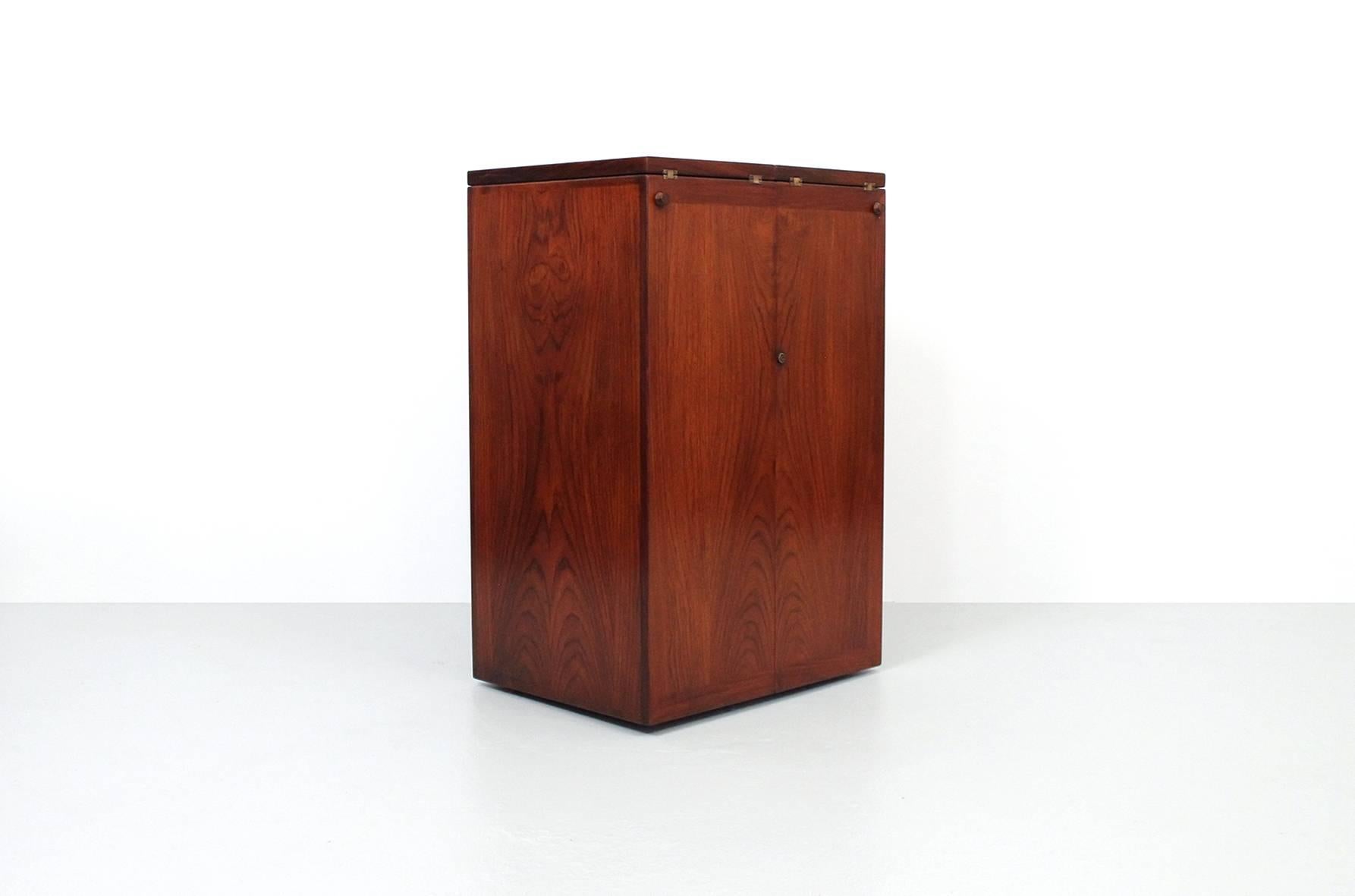 Hinged rosewood dry bar or cabinet designed by Reno Wahl Iversen for Dyrlund. This bar features numerous cubbies and drawers in addition to a top that unfolds to reveal a long surface of black laminate for drink preparation. Beautiful brass hardware