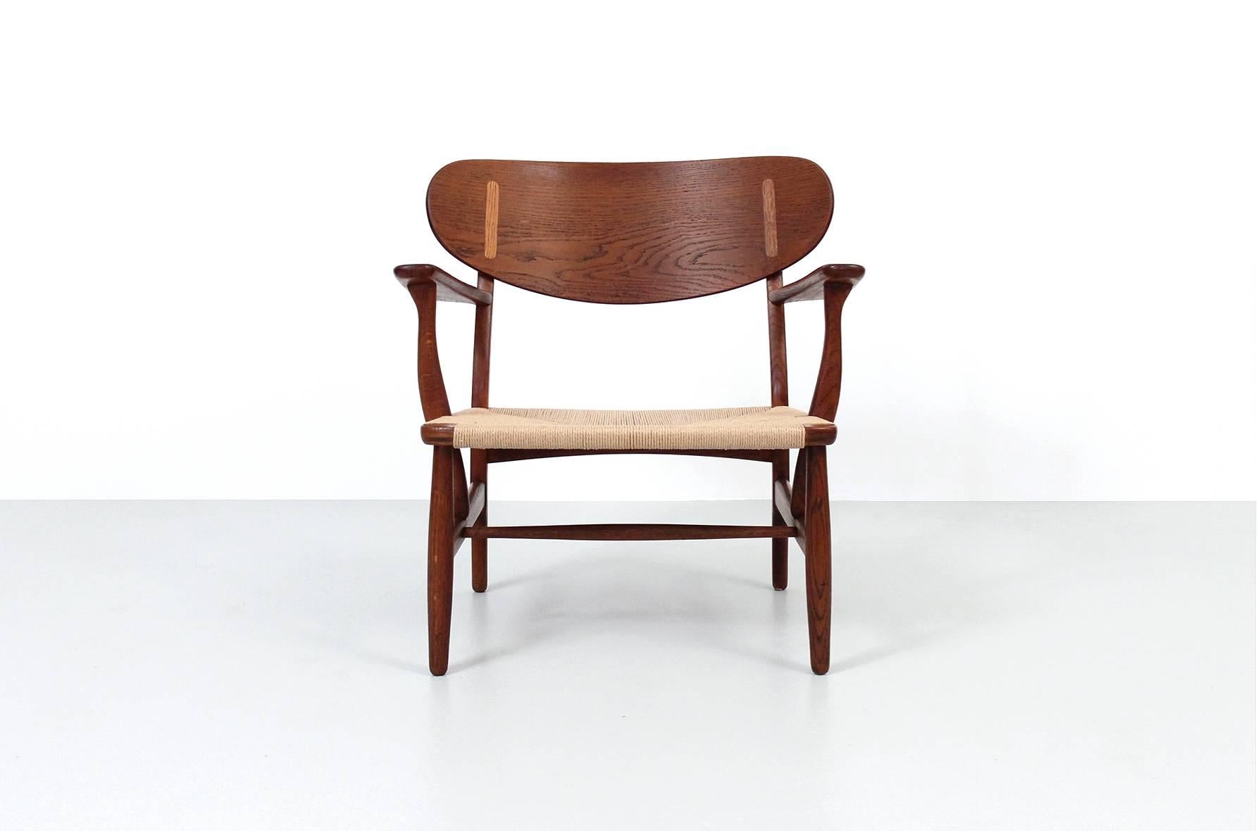 Early pair of CH22 lounge chairs by Hans Wegner for Carl Hansen & Søn. Handsome and sculptural chair design from 1951 executed in oak with woven papercord seats.