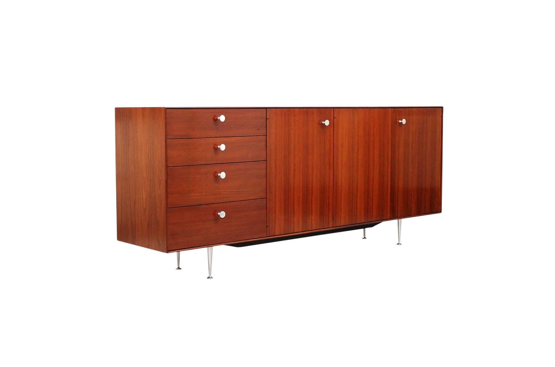 Walnut thin edge cabinet designed by George Nelson for Herman Miller. This is an early example of the series dating from circa 1960. It features four drawers and three doors, an interior cork lined drawer, and steel pulls and legs.
 