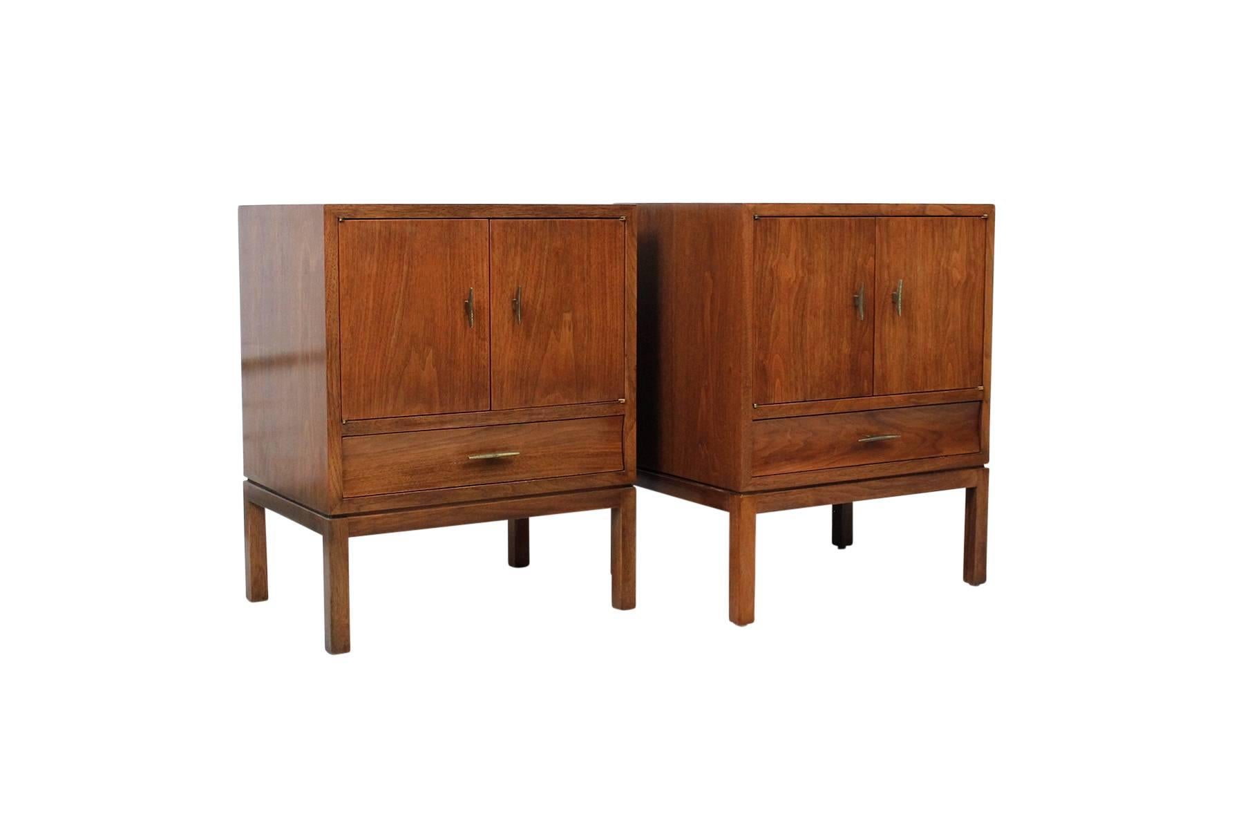 Pair of nightstands by American designer Edward Wormley for Dunbar. These nightstands feature oiled walnut cases, brass pulls, and white laminate drawer bottoms. Useful form with a variety of storage options. Labeled with brass Dunbar decals in the