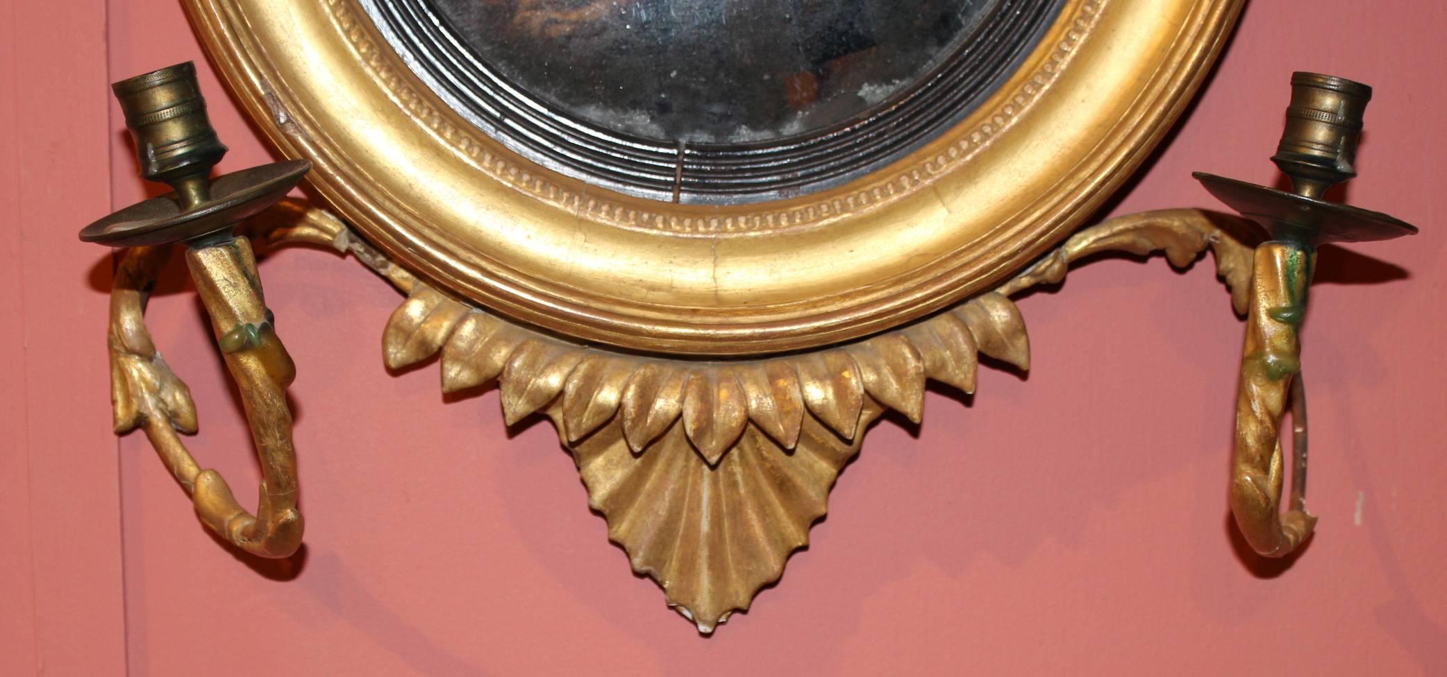 A rare example of a diminutive English giltwood girandole convex mirror with acanthus decoration and simple molded frame with ebonized reeded interior surrounding the original mirror plate. Scrolled wire and gesso candle arms with brass cups and