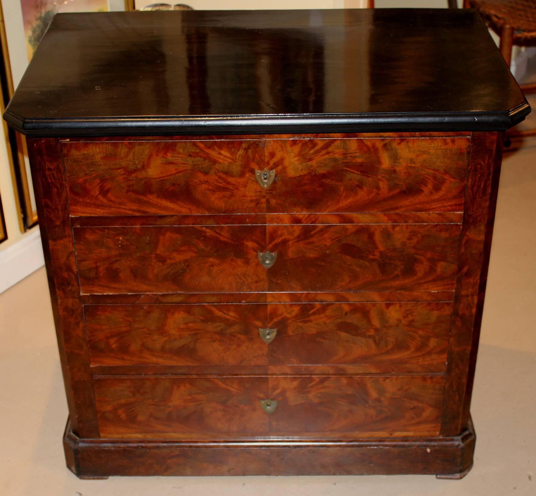 This near pair of 19th century Empire chests has book matched mahogany drawer fronts, chamfered corners, ebonized wooden tops, and brass shield form escutcheons and molded bases. 