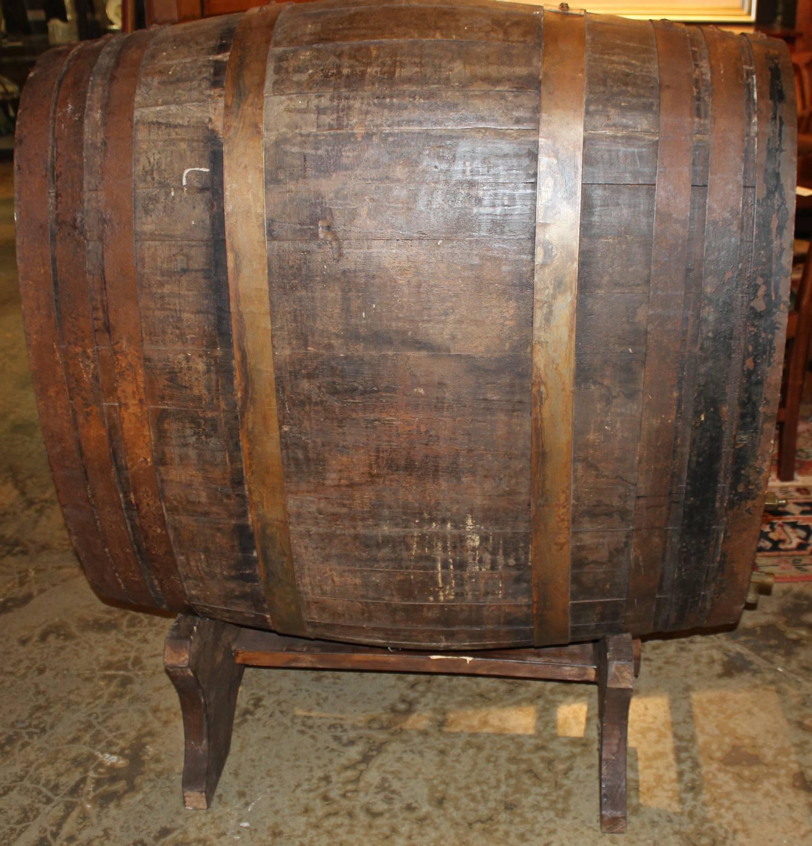 An oversized oval iron bound wine or champagne barrel / cask fitted with brass spigot, one end paint decorated with the numeral “7” above a cream colored cartouche labeled “Veuve Clicquot,” and fitted to a cradle Stand. Dates to the late 19th or