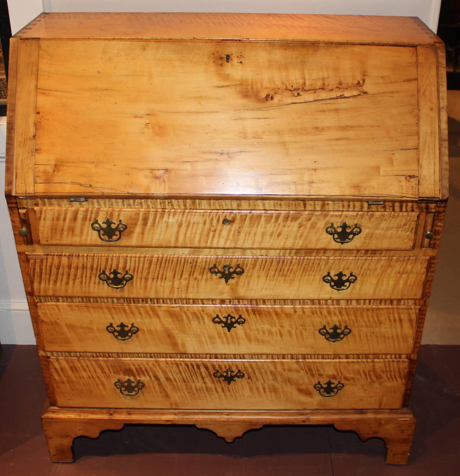 A tiger maple slant front desk, the lid opening to reveal a nicely compartmentalized interior featuring a round fan carved prospect drawer, all over four graduated drawers and raised on a nicely shaped bracket feet and centered by drop pendant.