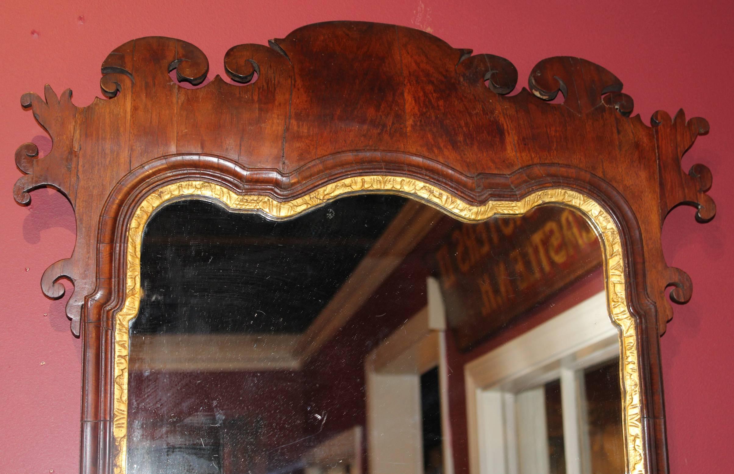 A fine example of an 18th century English Chippendale mahogany veneered looking glass or mirror with gilt decoration and delicately carved scrolled frames.