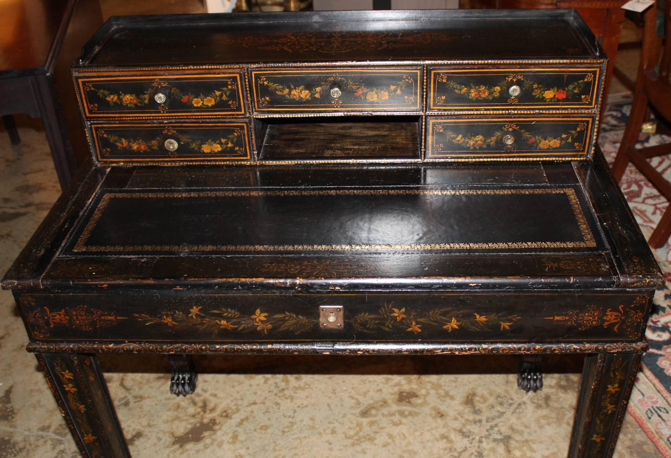 A fine polychrome writing desk in black lacquer with a five fitted drawer gallery, leather sliding writing surface with gilt border over a single frieze drawer, supported by tapered square legs terminating with paw feet. All with hand painted floral
