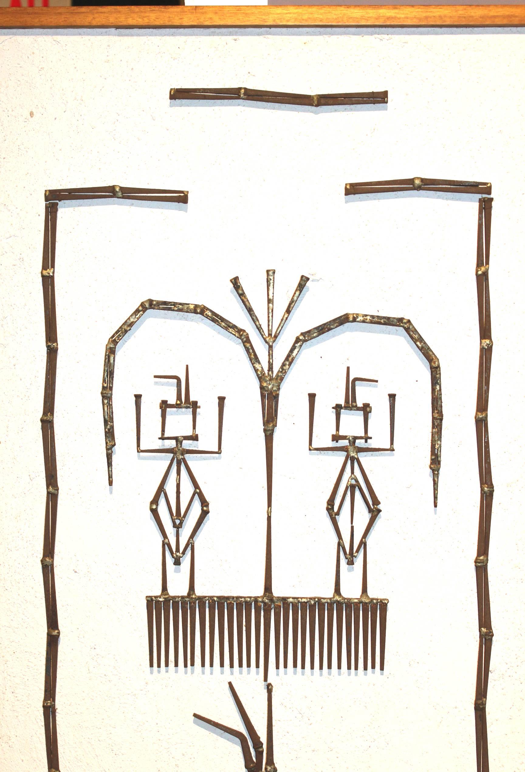 This Mid-Century Modern wall art is composed of plaster on wood, with welded square nails depicting two figures under a tree, unsigned and framed in a simple wood frame.