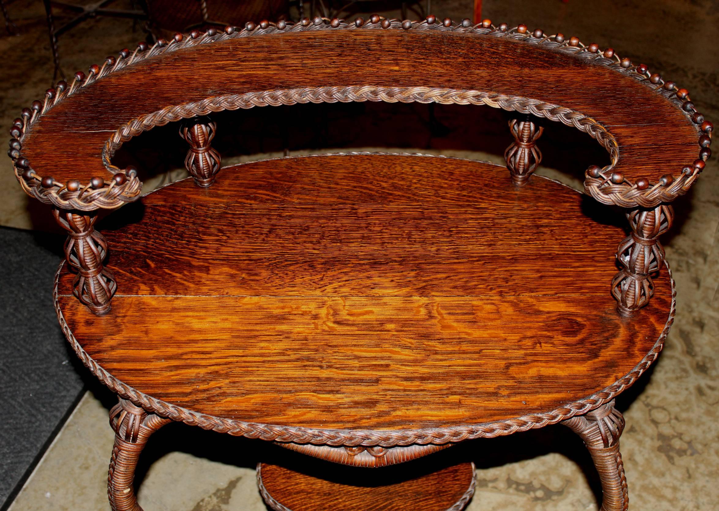A superb example of a wicker and oak two-tier oval side table with crescent shaped oak top tier and table top. A Heywood Bros & Co, Gardner MA paper label affixed on underside.\
 