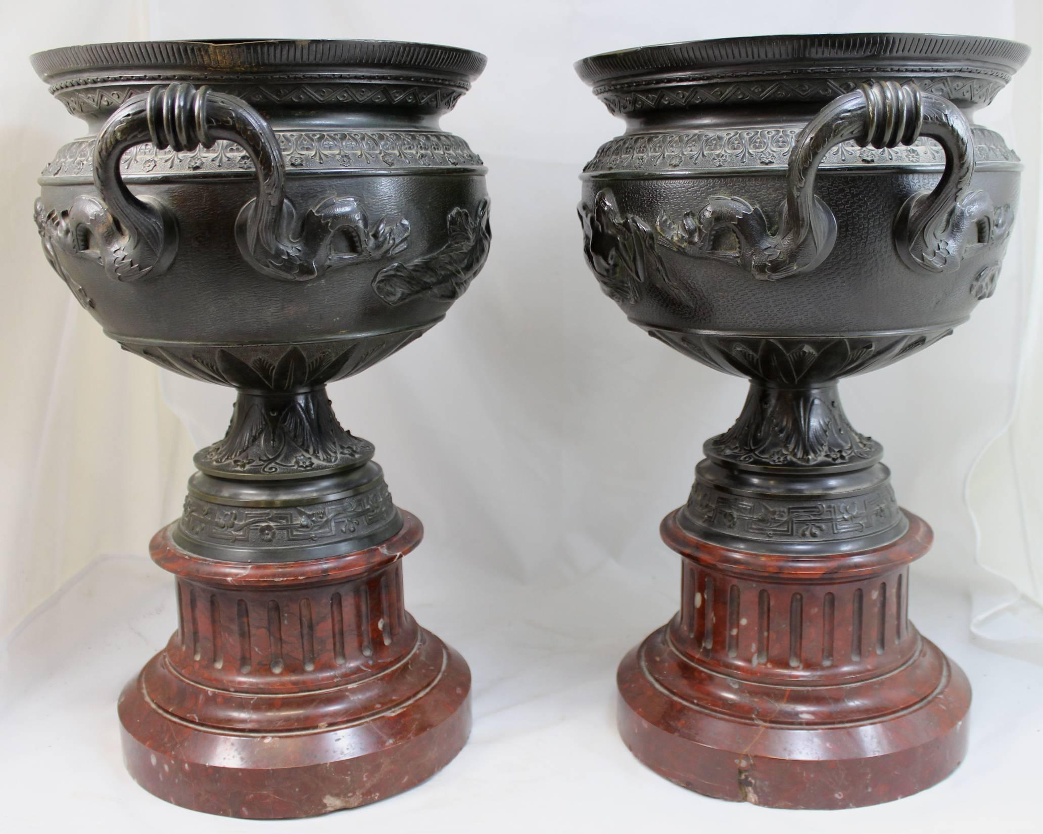 An exceptional pair of finely cast French bronze handled urns depicting Classical female figures, along with dragon or serpent decorated handles, with foliate and geometric designs, and mounted on Griotte Uni marble plinths, dating to second half of
