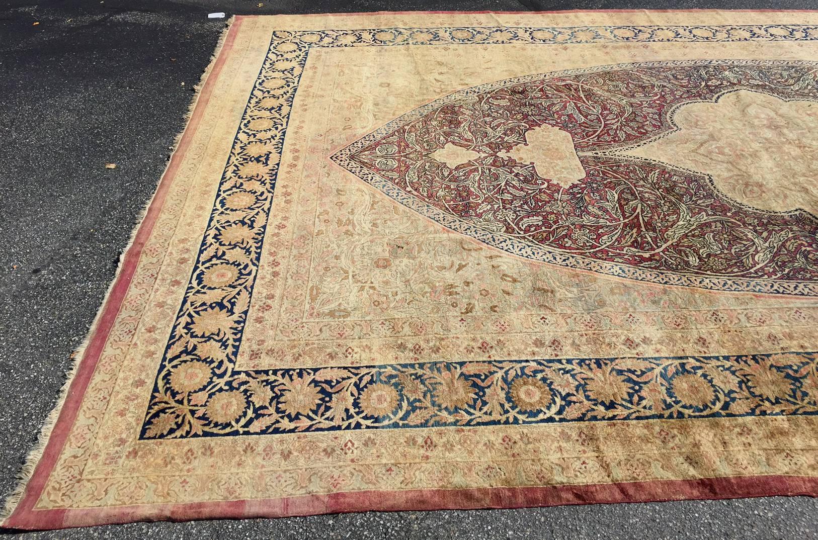 A fine example of an early 20th century large Imperial Royal Kerman handwoven rug with maroon oval center medallion with geometric center design on a sand or camel field with navy blue decorative border and muted red or pink outer border. These