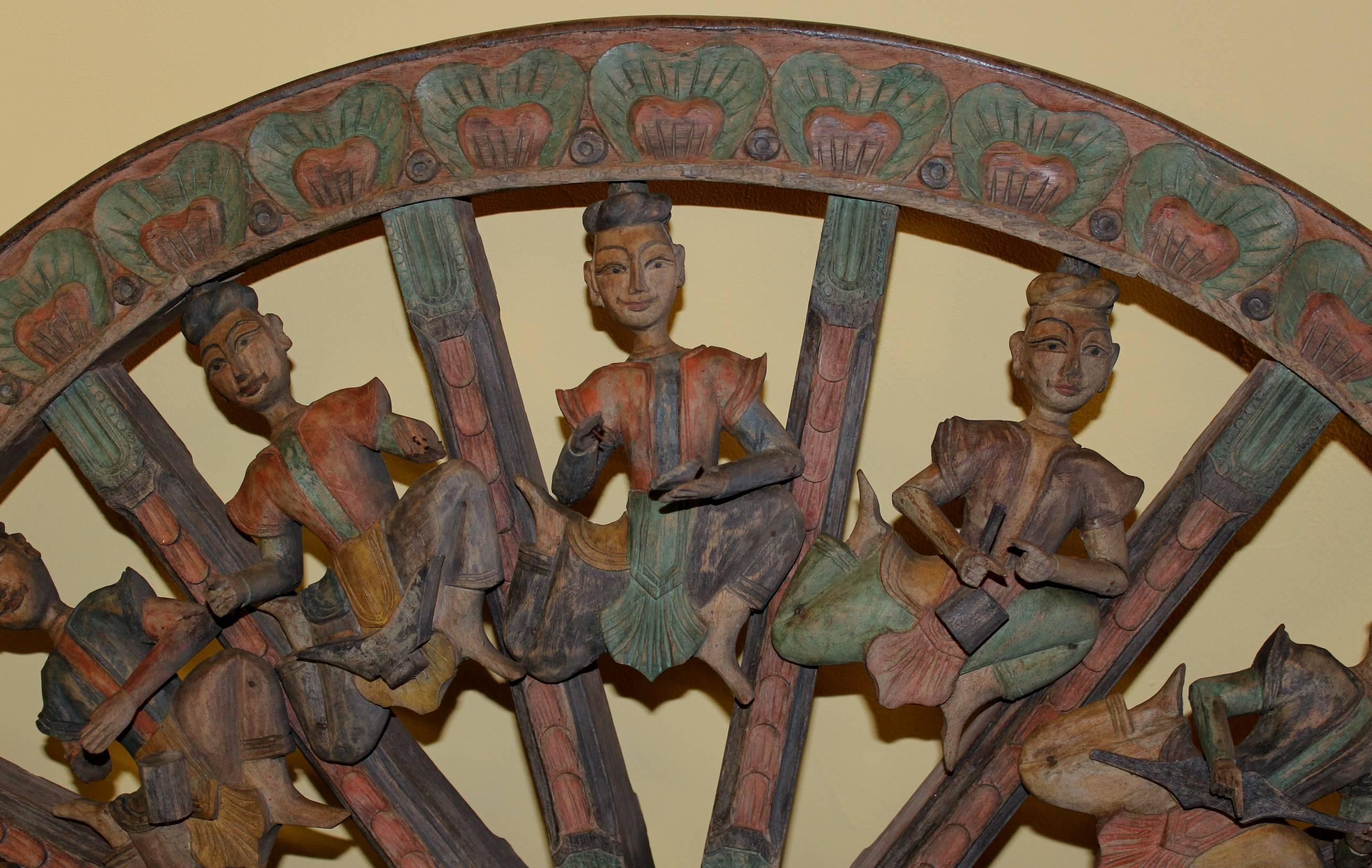 A polychrome wooden parade or carnival cart wagon wheel with a variety of carved three dimensional figures playing musical instruments as decoration between the foliate carved spokes and outer rim, which is lined with an iron band. Probably