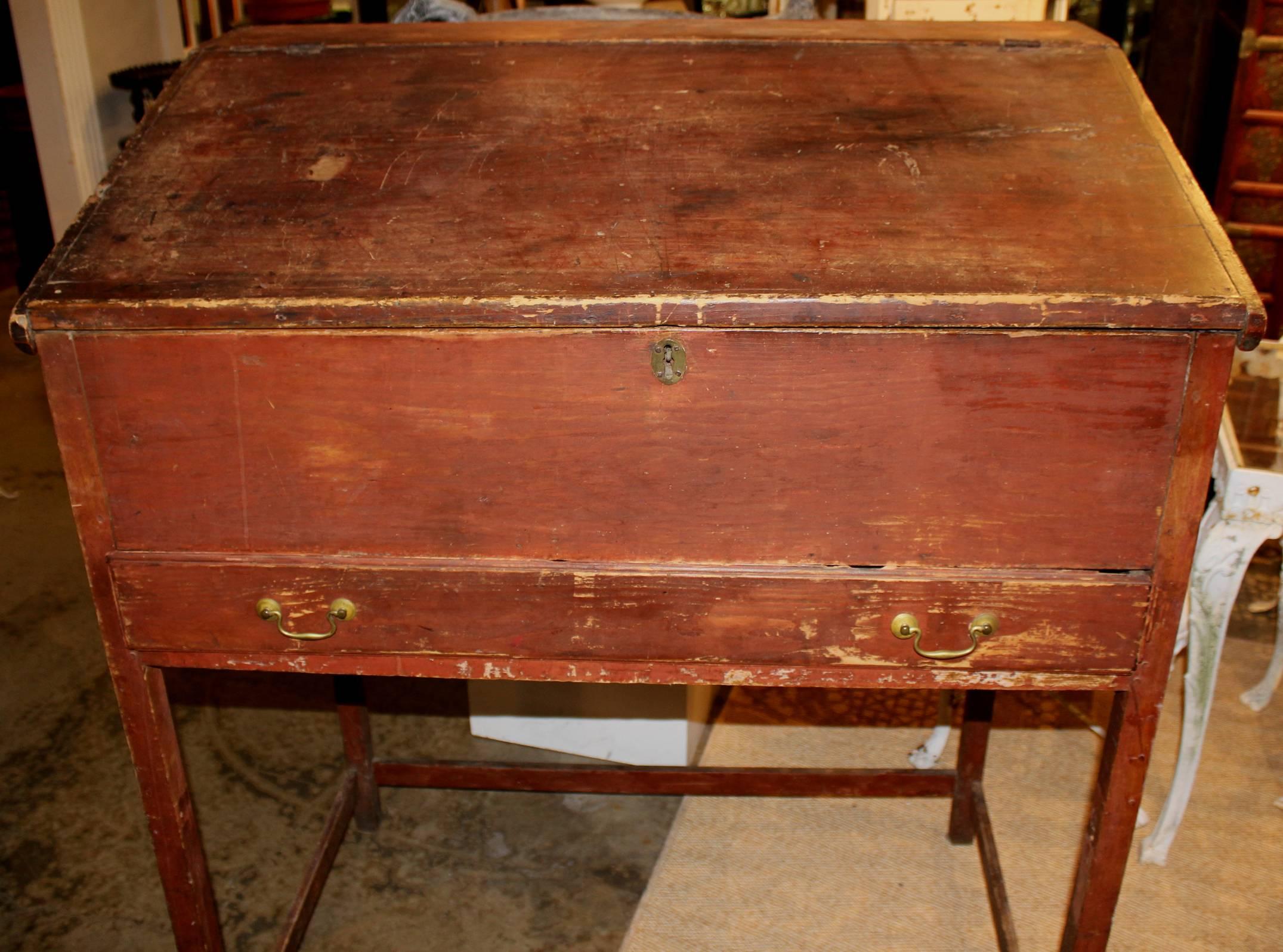 A fine example of a pine one drawer schoolmaster’s desk in its original old red paint with slanted lift top which opens to reveal an open compartment interior. Great patina with some interior ink staining.