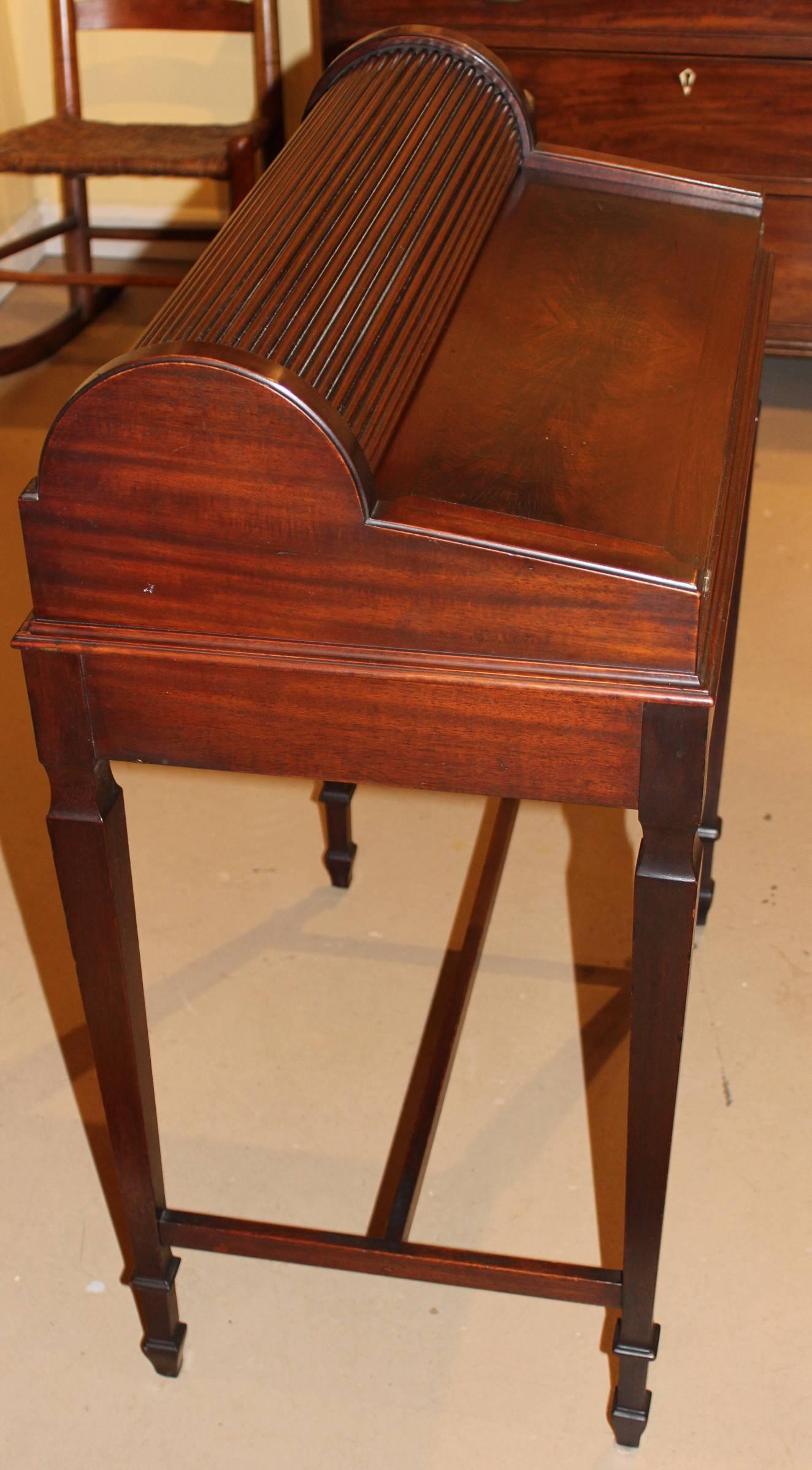 A unique writing desk with book-matched mahogany veneers has a petite upper roll top, which opens when the long locking fitted drawer is opened, to reveal a compartmentalized interior including a pen rail, fitted glass octagonal ink well with brass