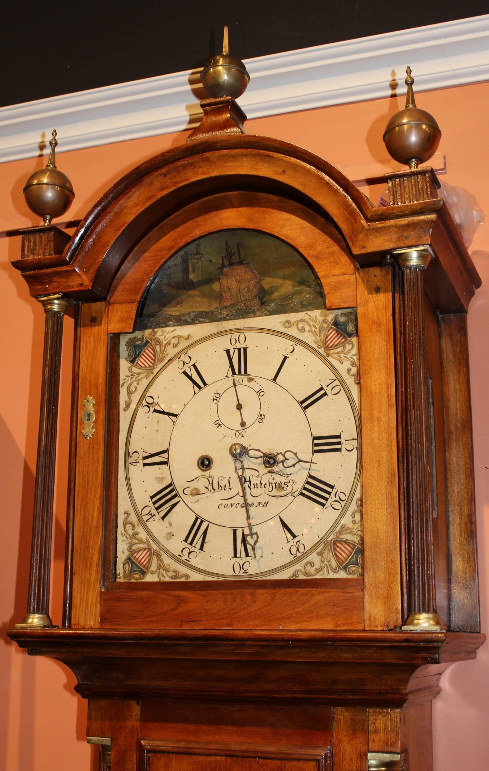 This exceptional New Hampshire tall case clock has a bonnet with arched molded cornice surmounted by three brass ball finials with spires above the arched door flanked by freestanding receded colonettes, fitted to the case above a cove molding