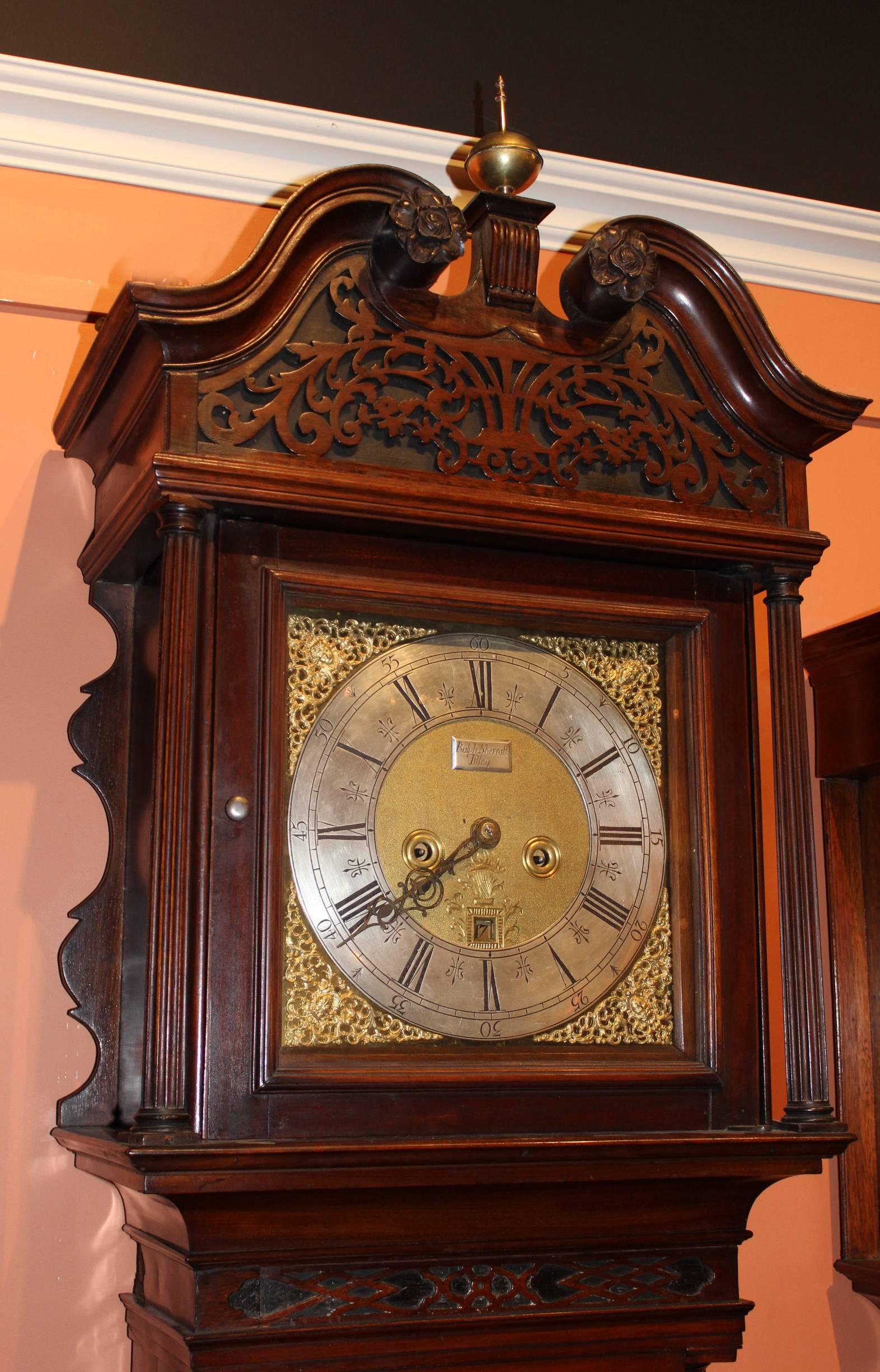 A Georgian Chippendale mahogany tall case clock, probably 18th century English, with carved swan neck broken pediment, around a single central brass ball finial with spire, fluted columns flanking the brass Roman numeral dial with matted center,