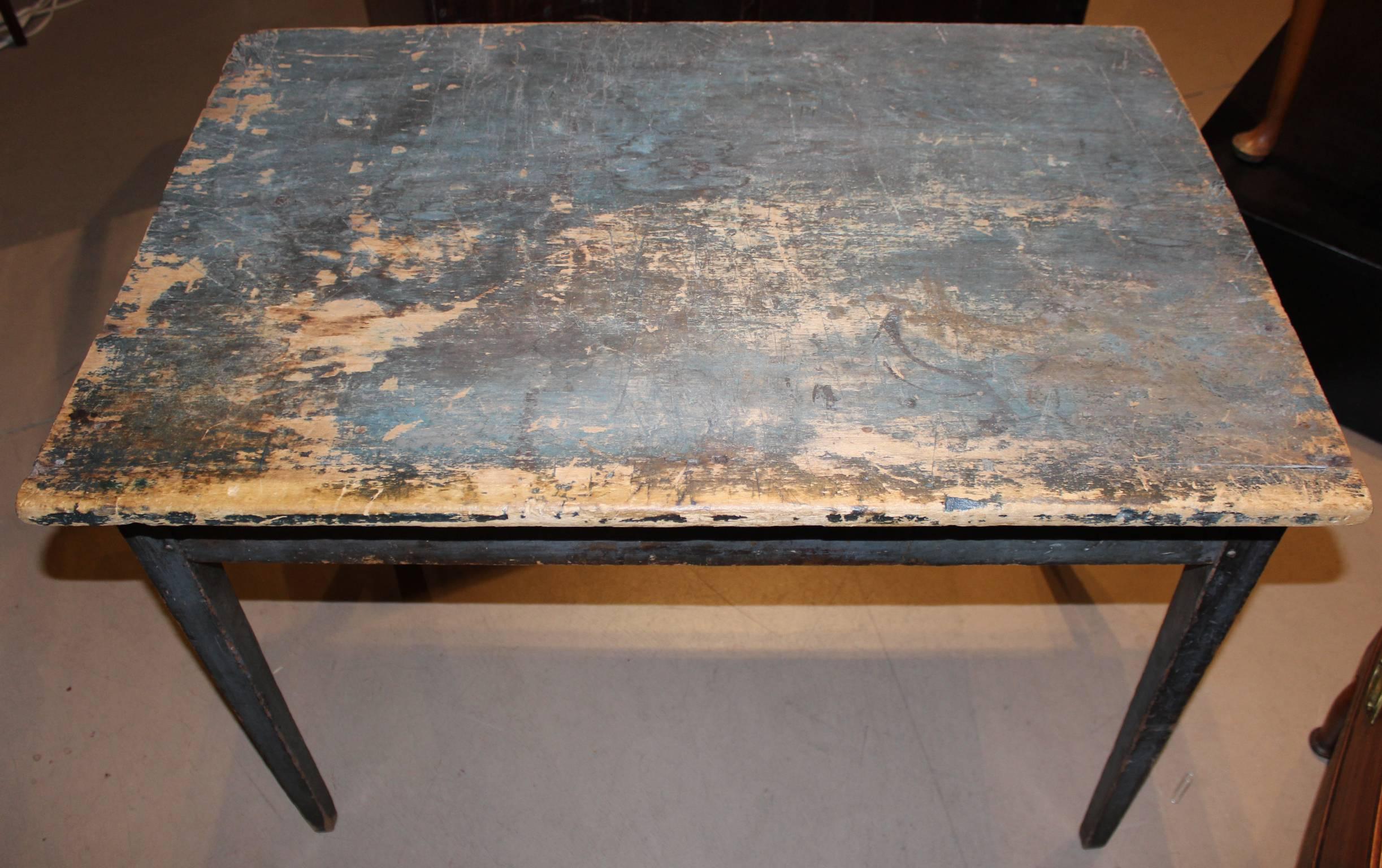 This early American pine work table circa 1820 in old blue paint has a great worn surface and nice Primitive look with patches of paint loss, discoloring in spots, and overall expected surface wear from age and use. The underside appears unpainted.